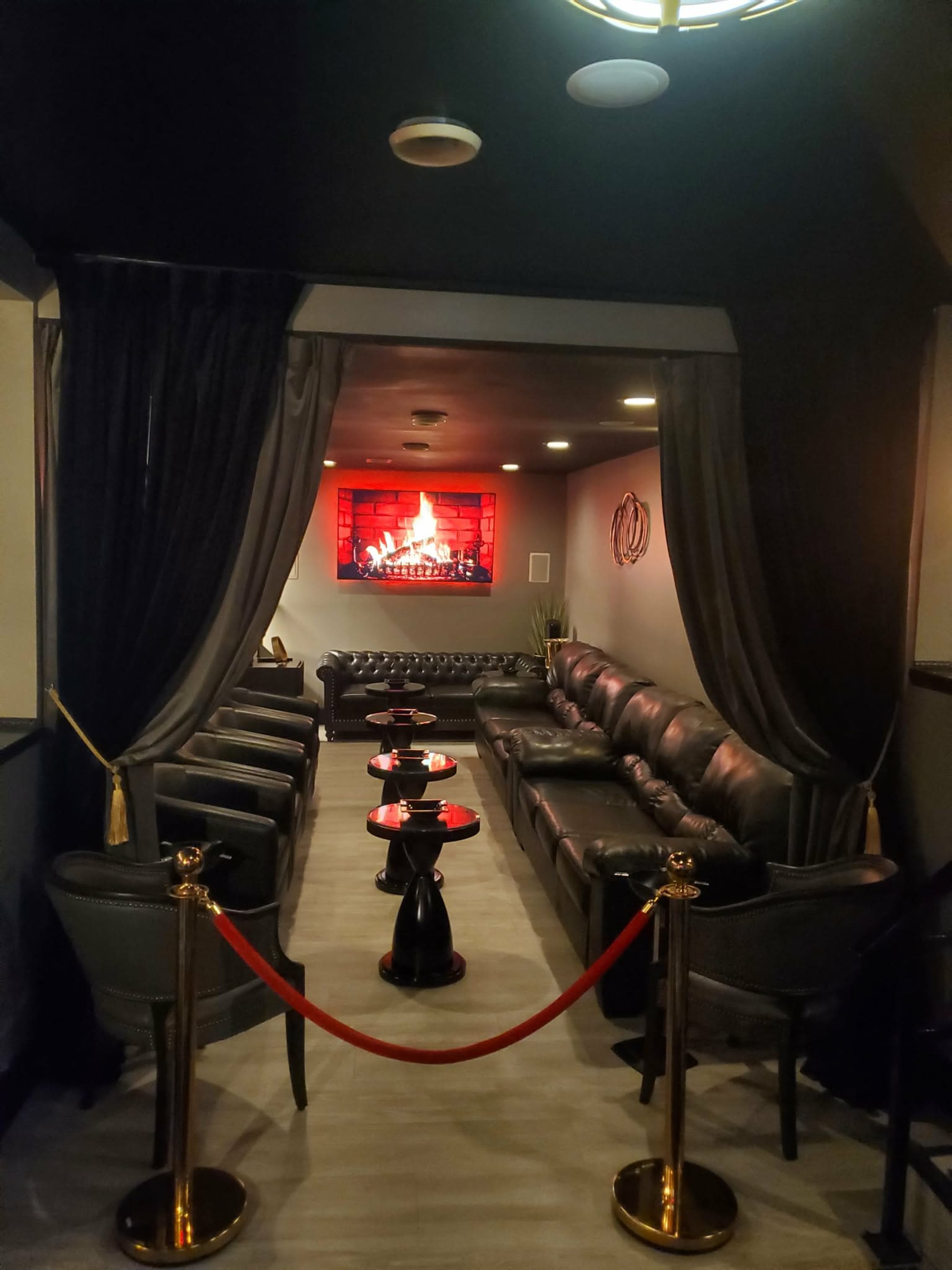 The image shows a cozy lounge area with black leather sofas, a decorative fireplace on the wall, and small tables arranged in front of the seating.