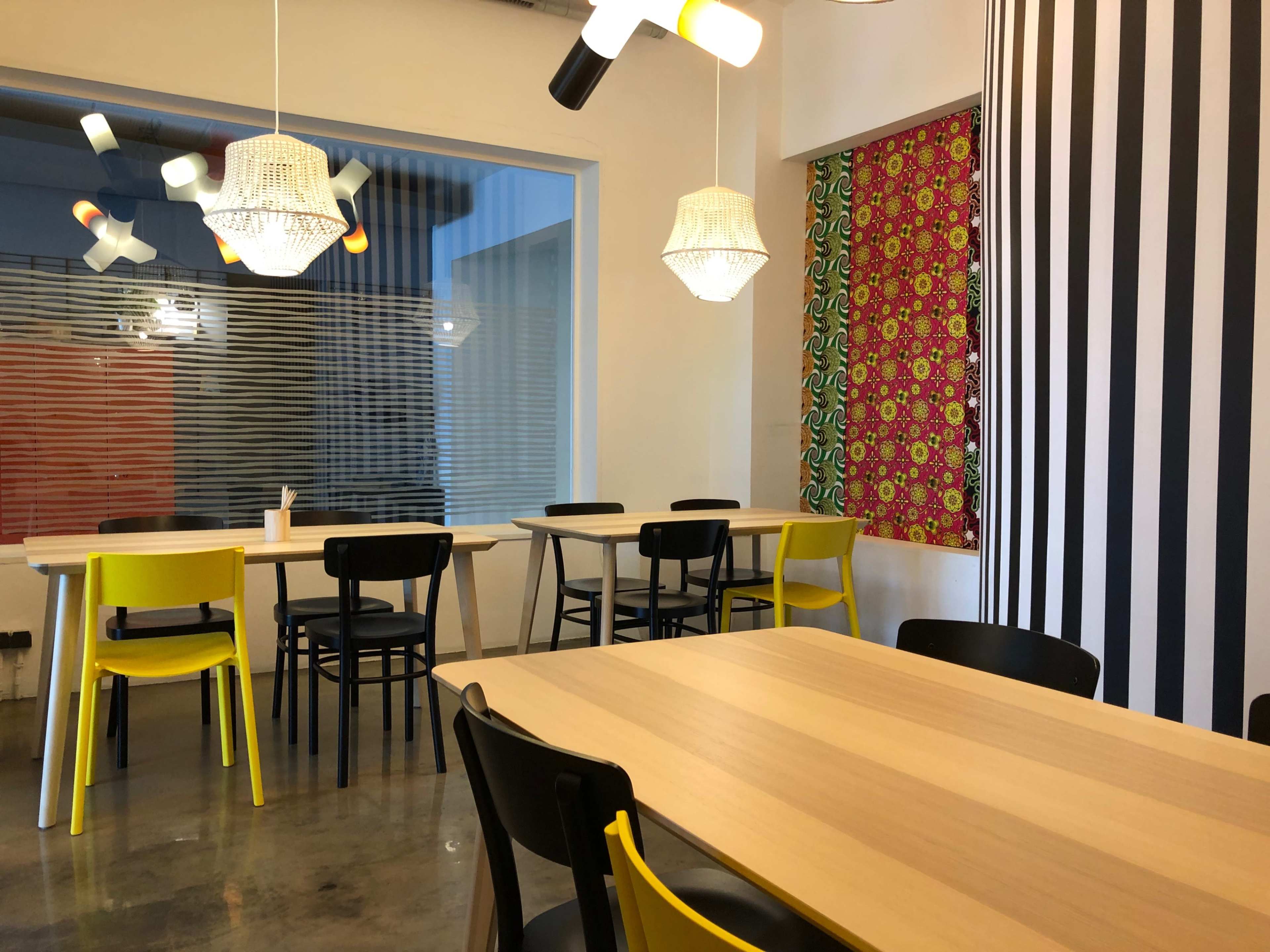 A modern dining area with wooden tables and a mix of yellow and black chairs, accompanied by decorative wall elements and pendant lighting.