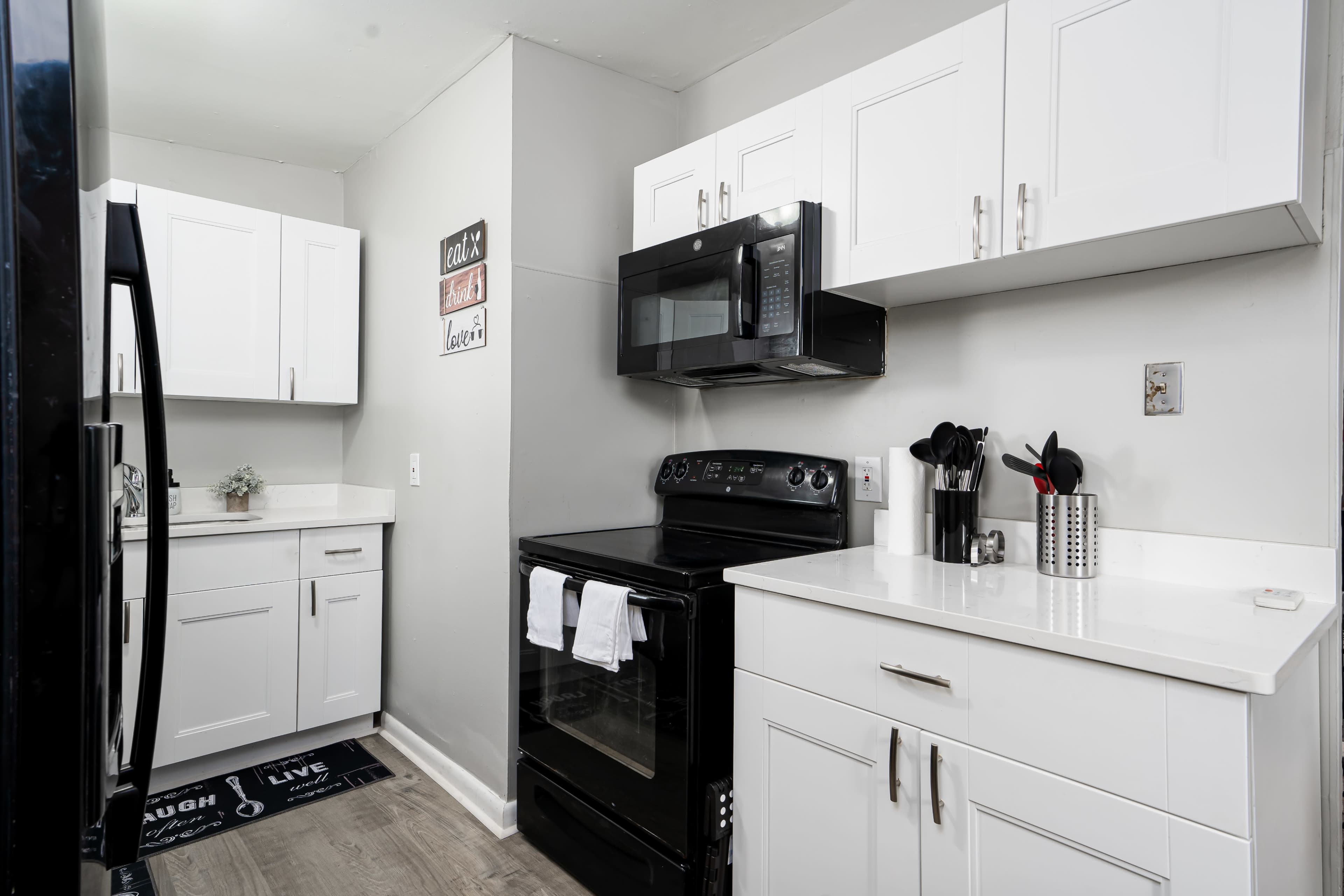 The image shows a modern kitchen with white cabinetry, a black stove and microwave, and a gray wall.
