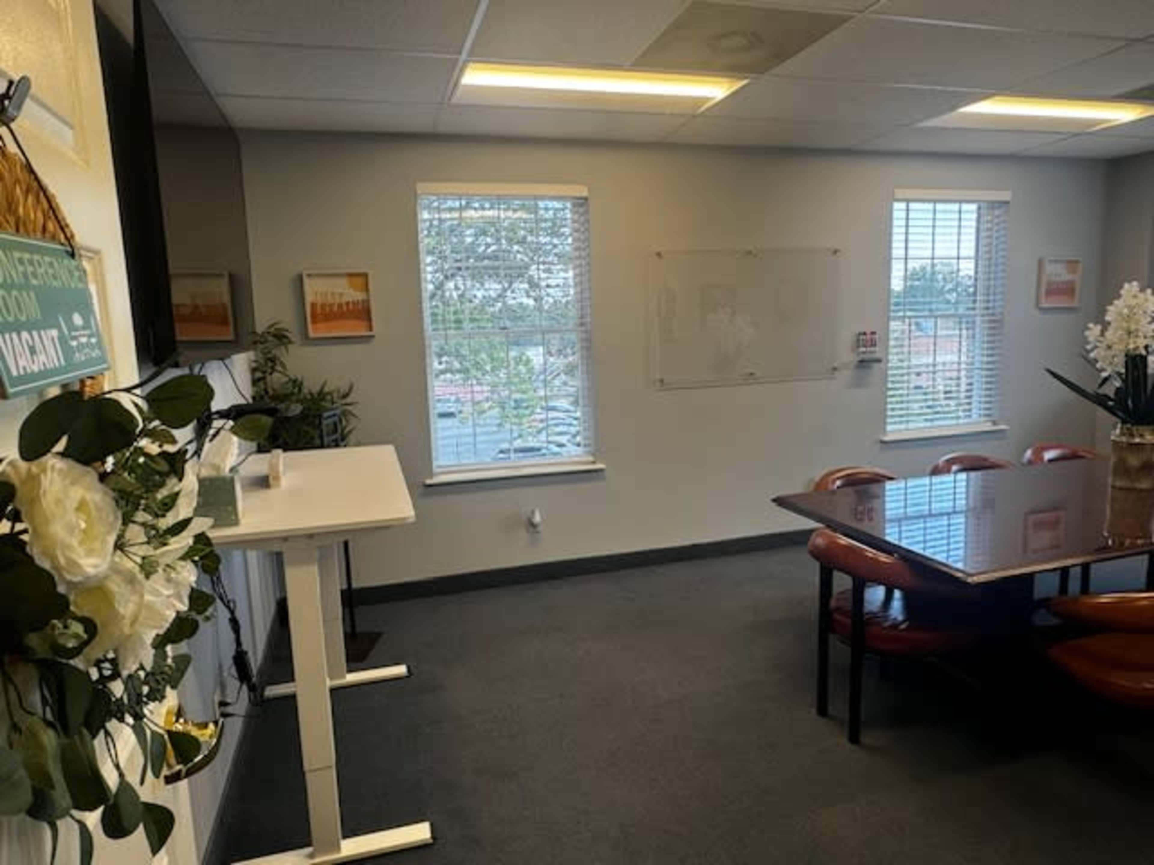 A meeting room with a large table, chairs, a whiteboard, and windows letting in natural light.