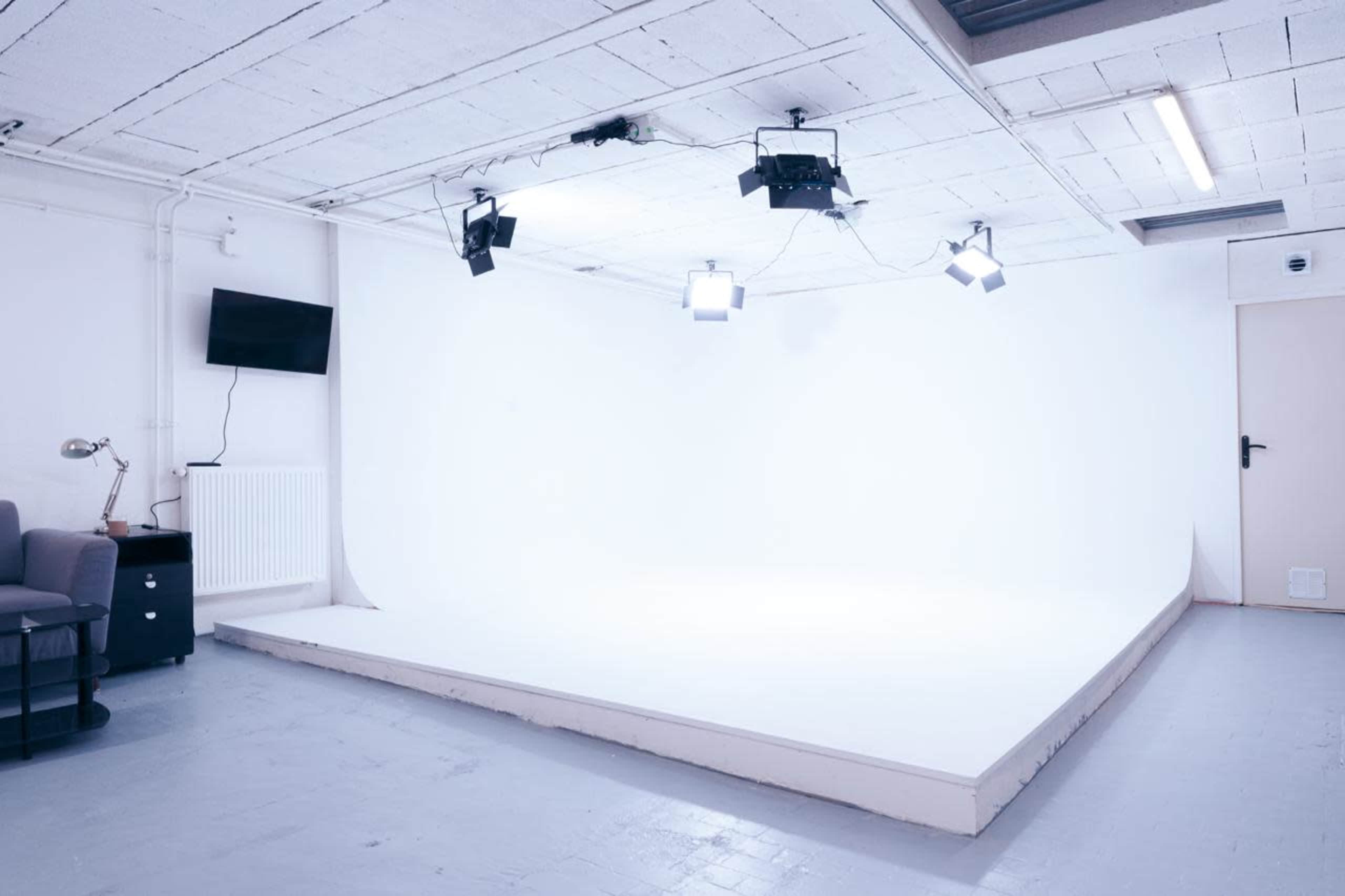 The image shows a well-lit photography studio with white walls and a blank backdrop.