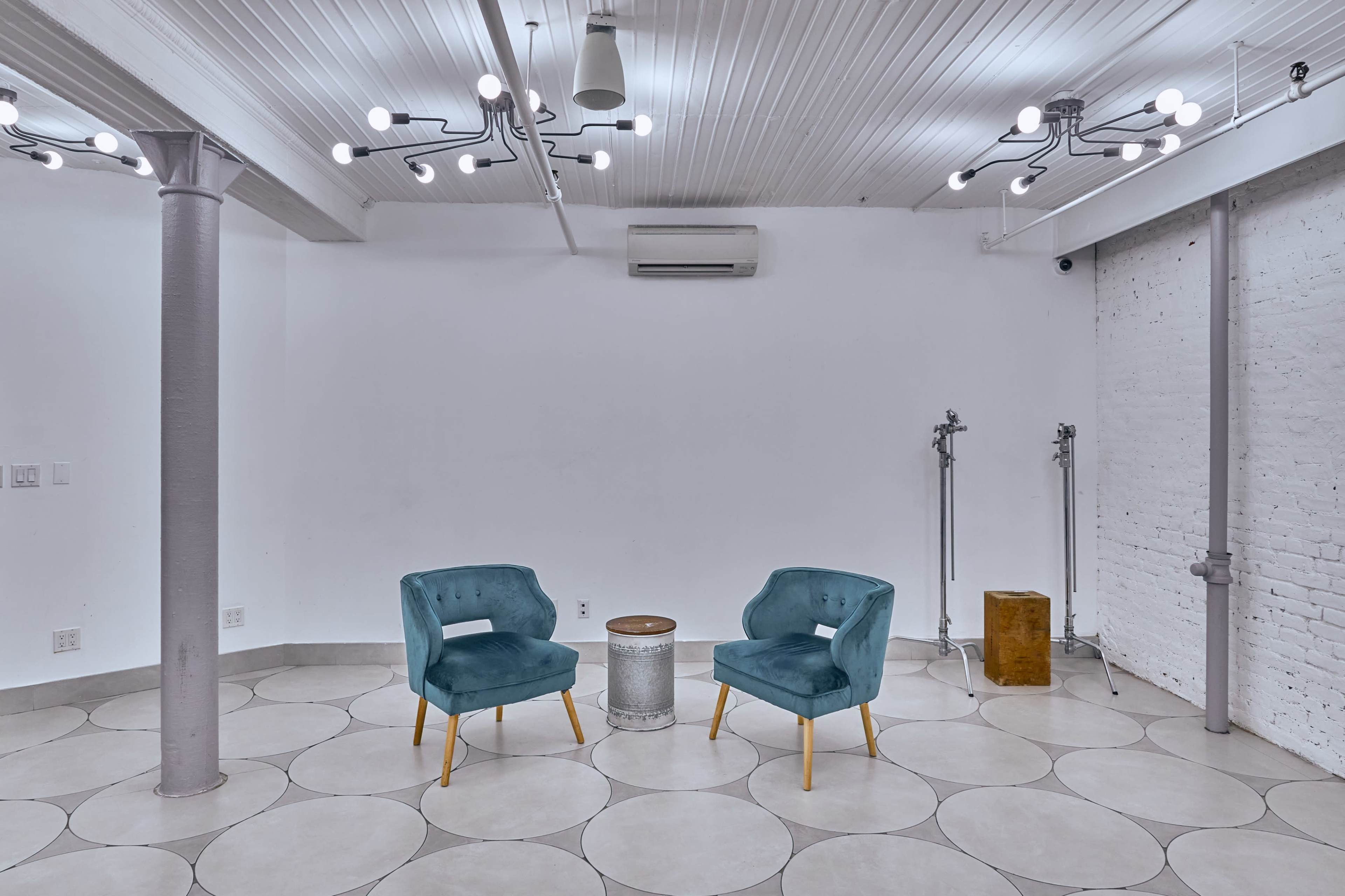 A minimalist room with two teal chairs, a small round table, and various overhead lights on a white ceiling.