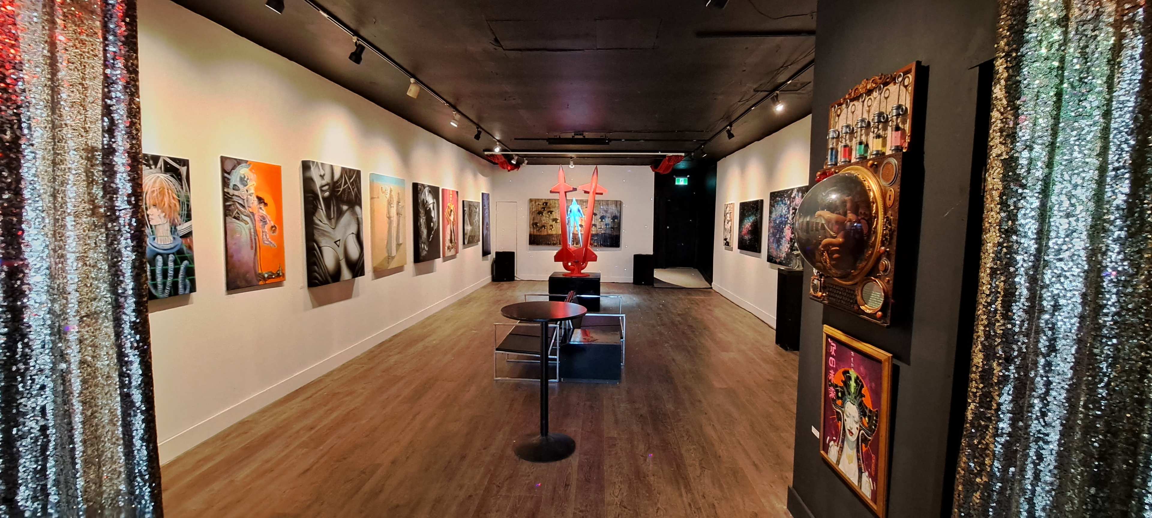 An art gallery hallway featuring colorful wall-mounted artworks, a central sculpture, and decorative elements along the entrance.