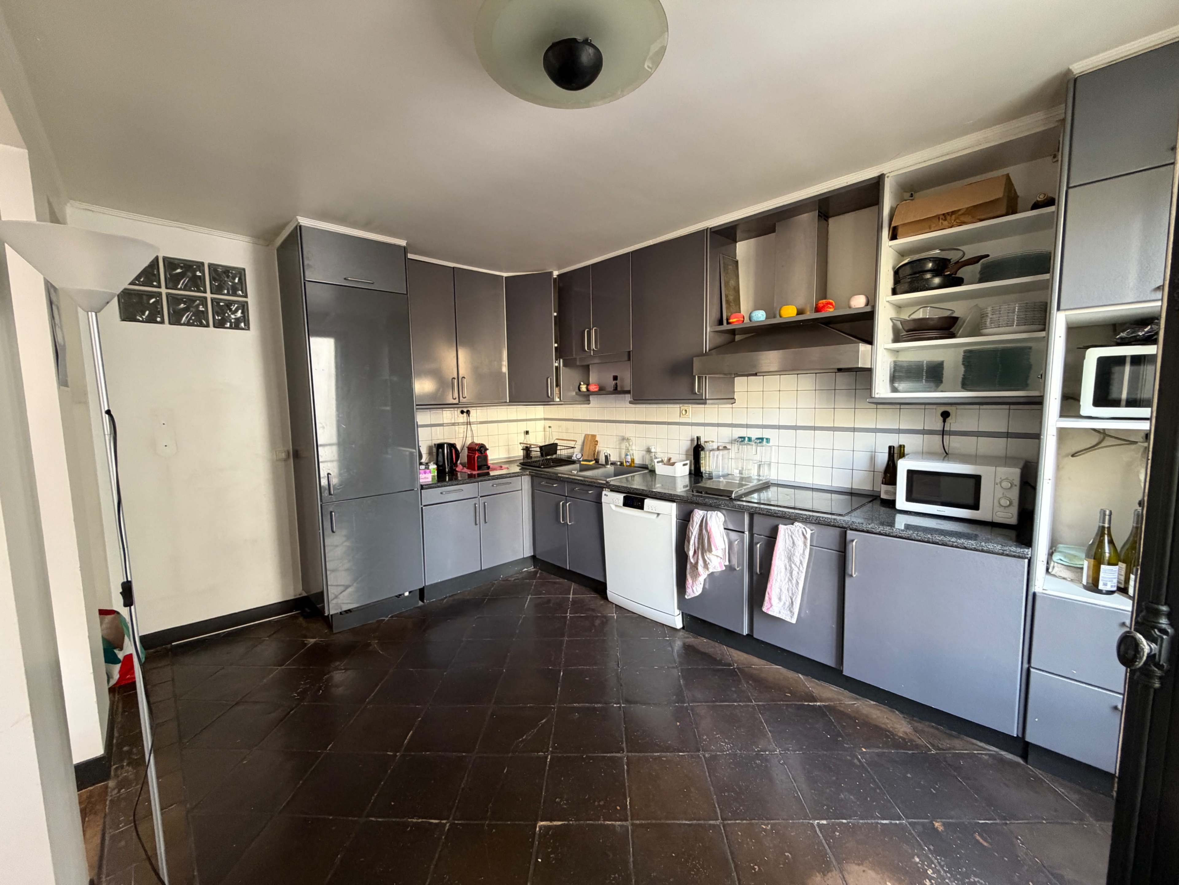 The image shows a modern, spacious kitchen with dark tiled flooring, gray cabinets, and various kitchen appliances visible on the countertops.