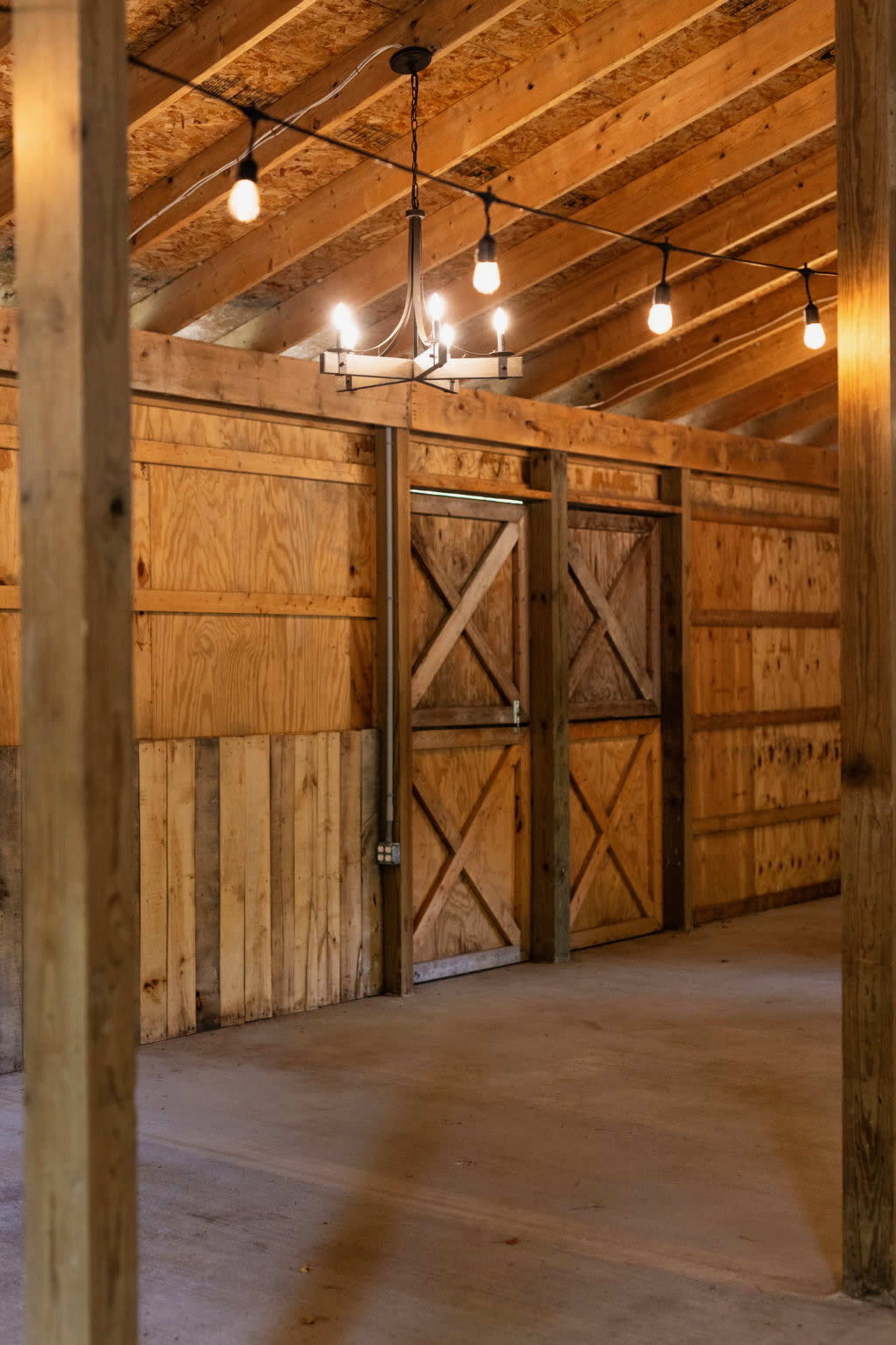 The image shows an empty room with wooden walls and a ceiling, featuring exposed light bulbs and double doors.