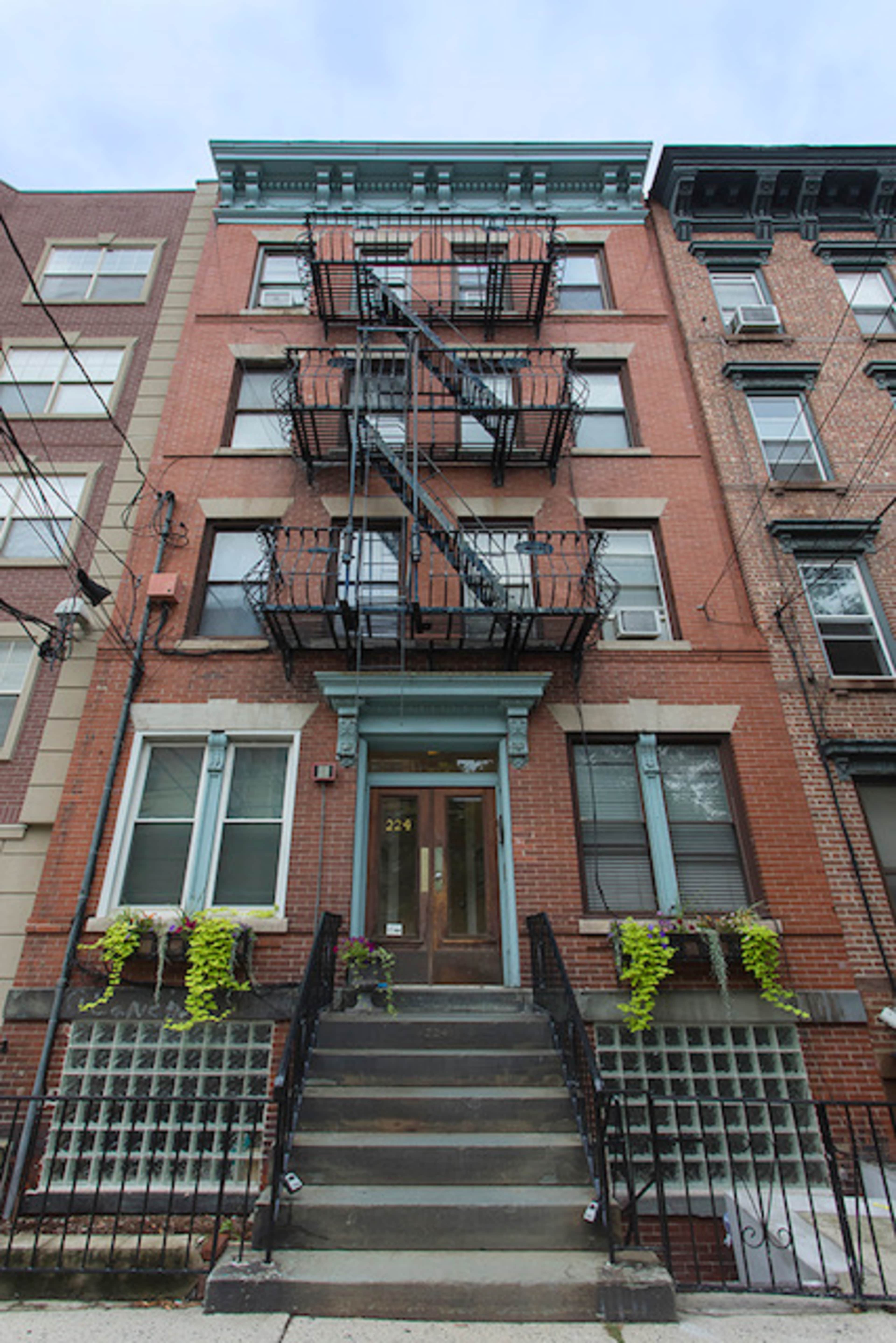 A brick building featuring a prominent staircase, metal fire escapes on the facade, and window planters.