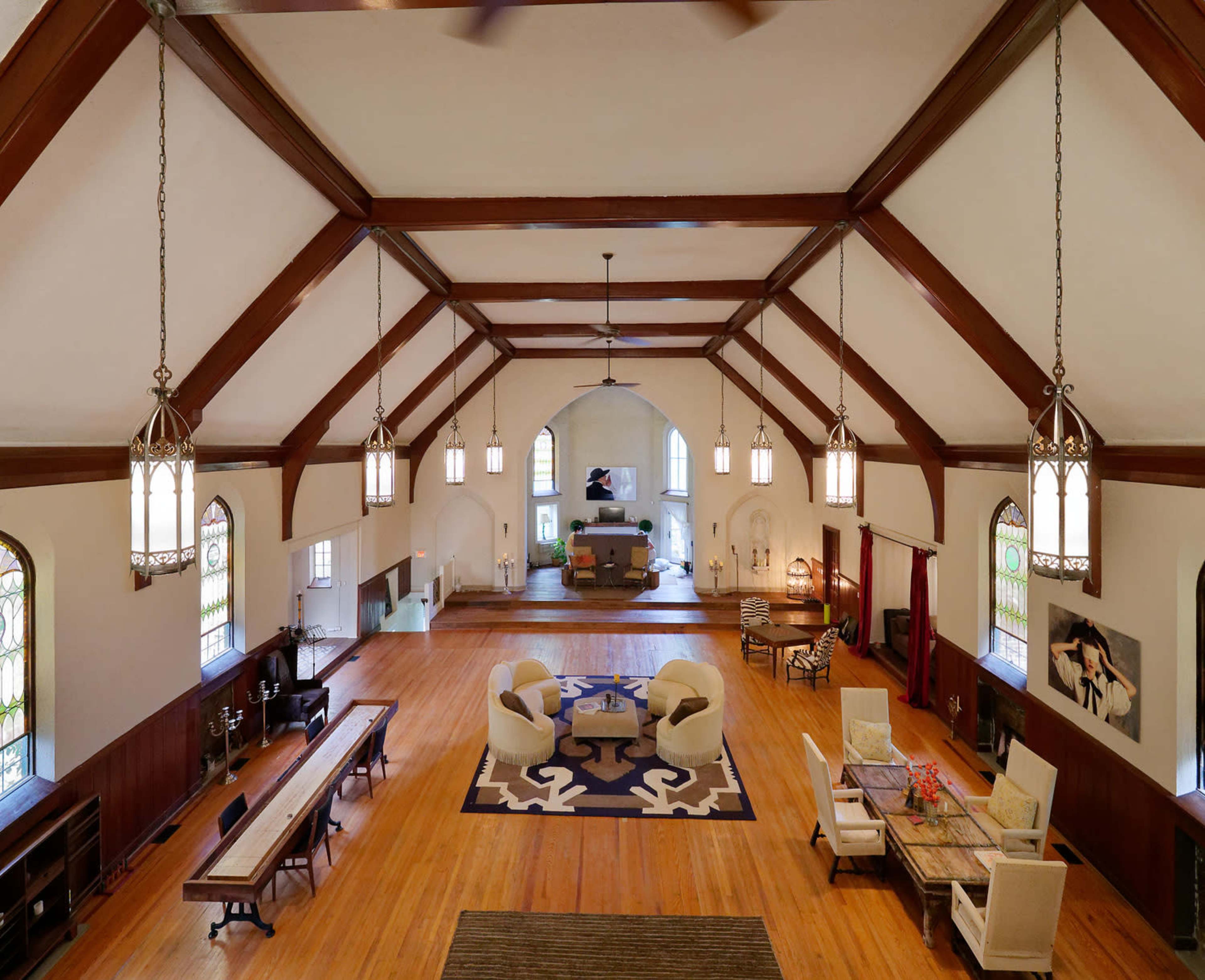A spacious interior of a hall with wooden beams, large windows, and a combination of seating areas and dining space.