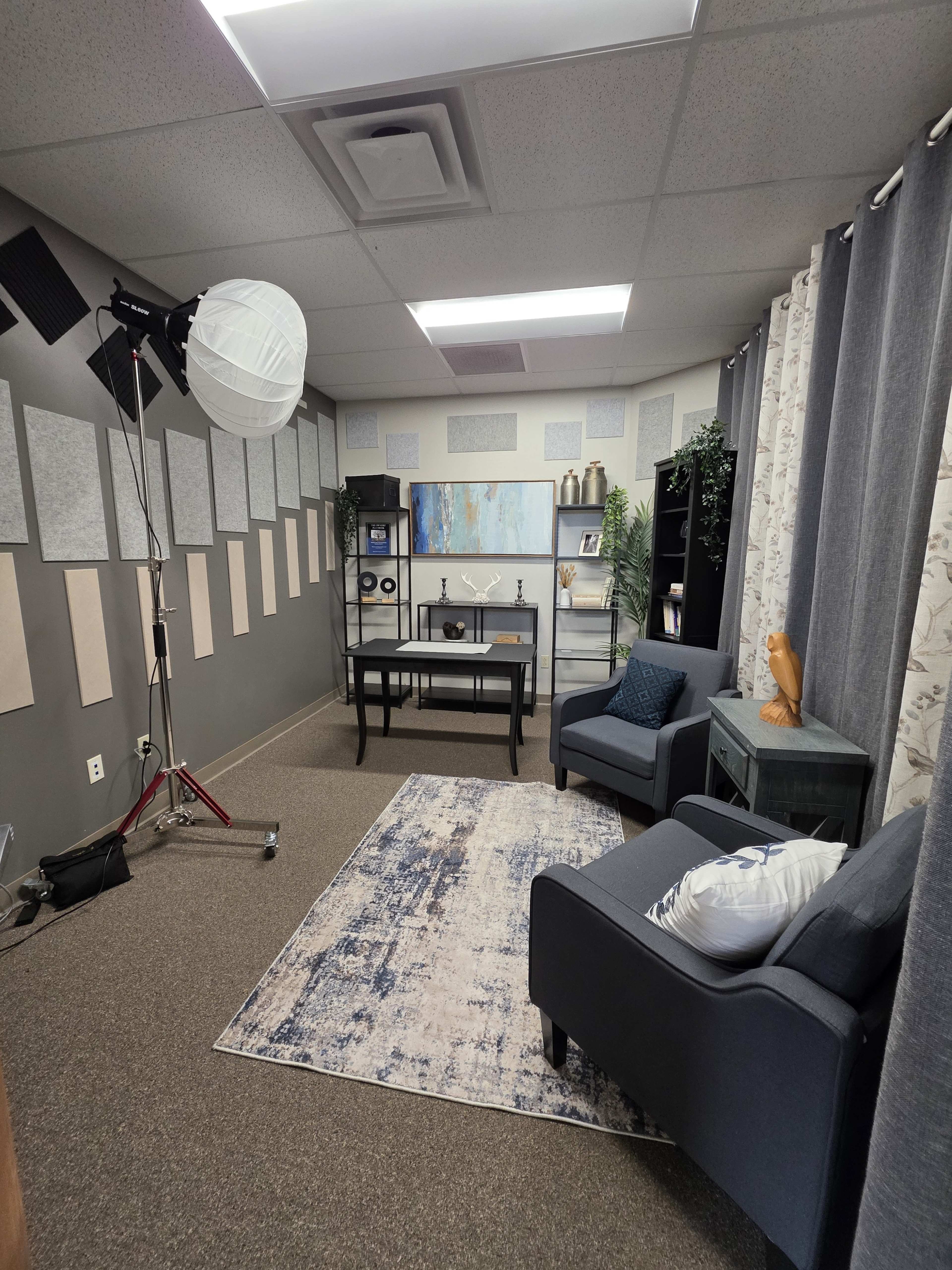 The image shows a small, professionally designed office or studio space with two armchairs, a desk, and soundproof panels on the walls.