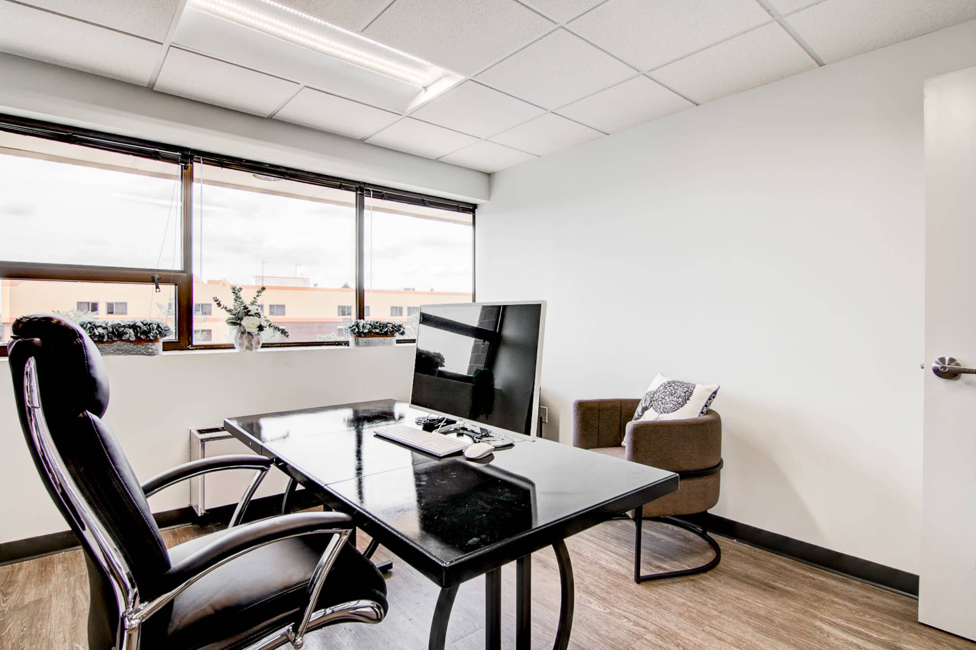 A modern office space featuring a black desk and a swivel chair, with a large window letting in natural light.