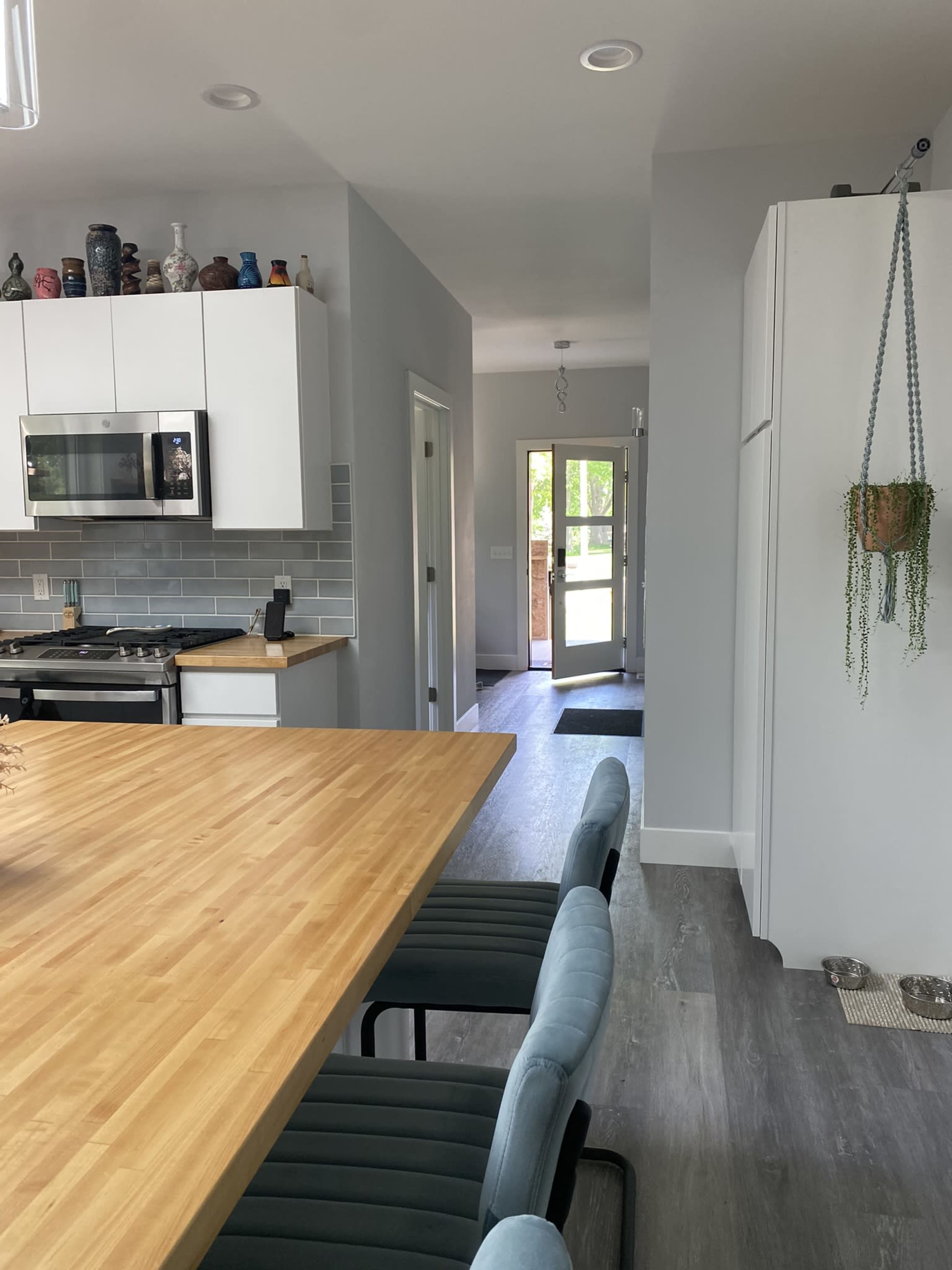 A modern kitchen and dining area with a large wooden table, light blue chairs, stainless steel appliances, and a doorway leading to an outside entrance.