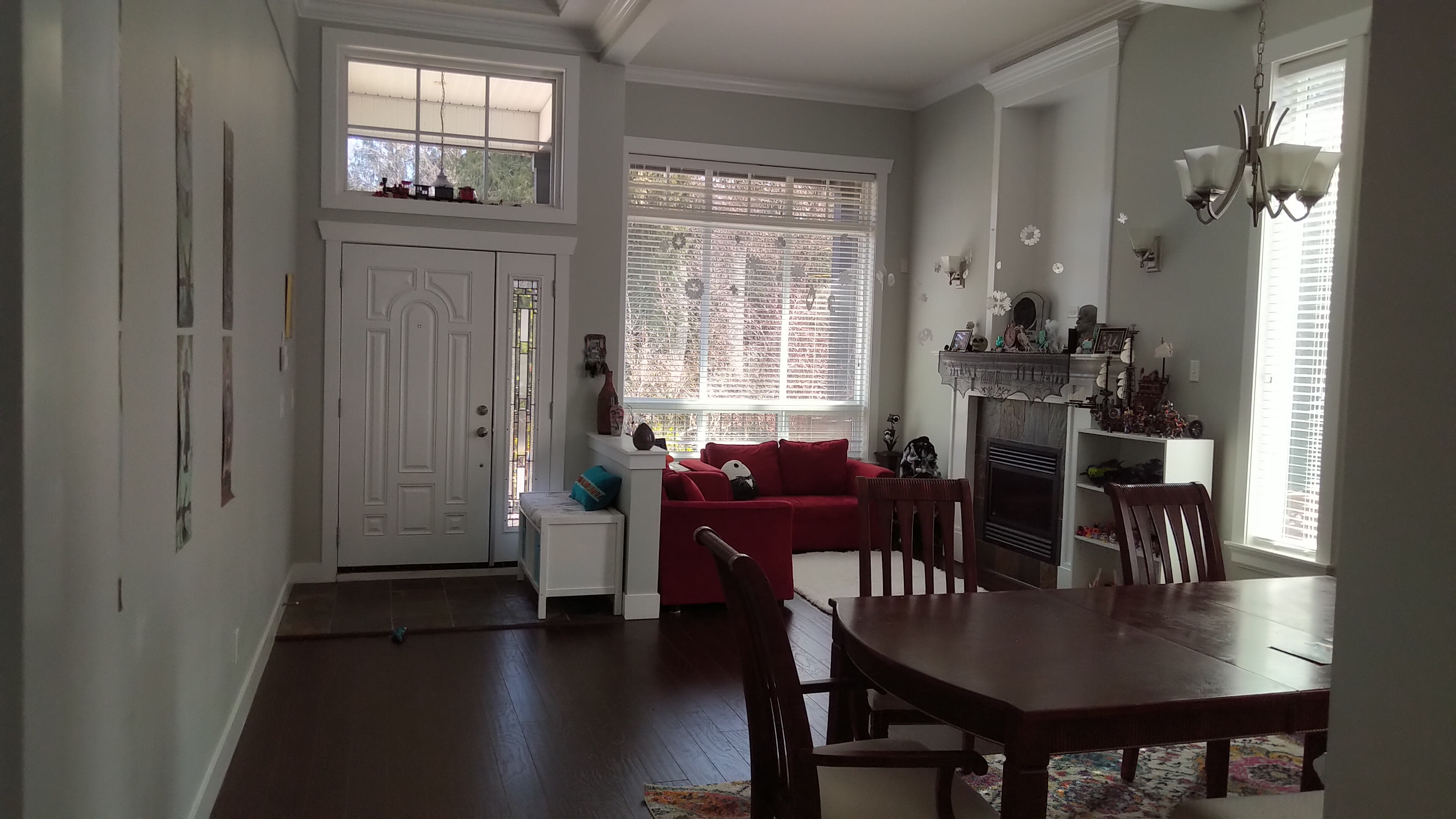 A living room and dining area with a front door, a dining table, and a red couch near a fireplace.