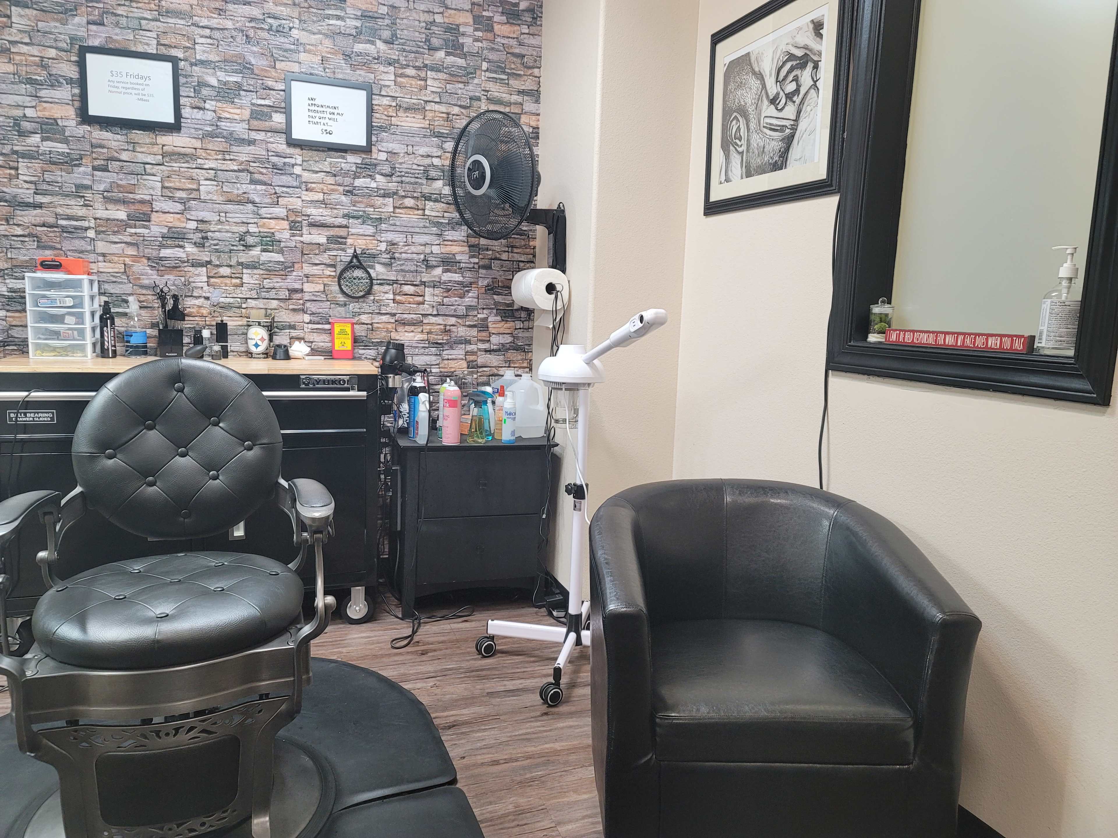 A dimly lit barbershop interior featuring a barber chair, a black armchair, and various grooming tools against a stone-patterned wall.