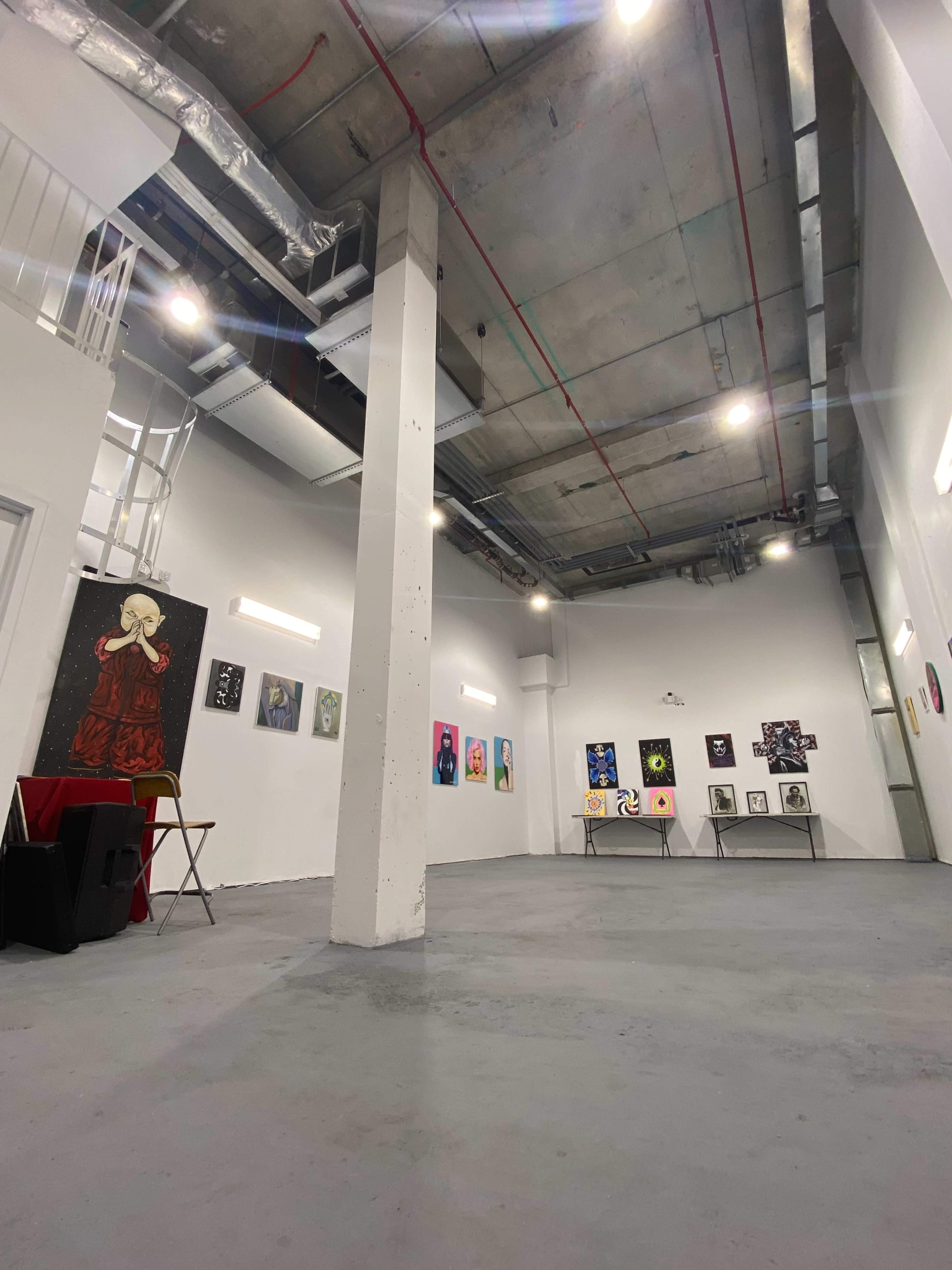 An interior gallery space with a polished concrete floor, featuring various artworks displayed on white walls under bright overhead lighting.
