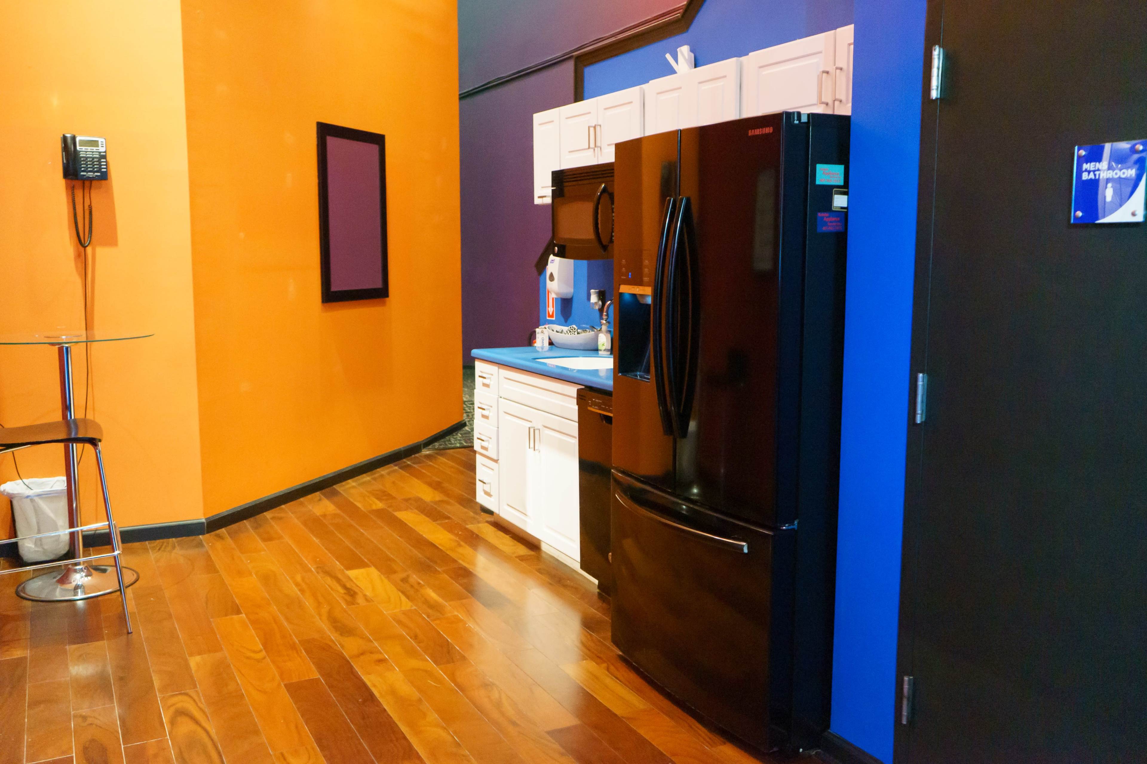 A modern kitchenette featuring a black refrigerator, white cabinetry, and an orange and blue wall.