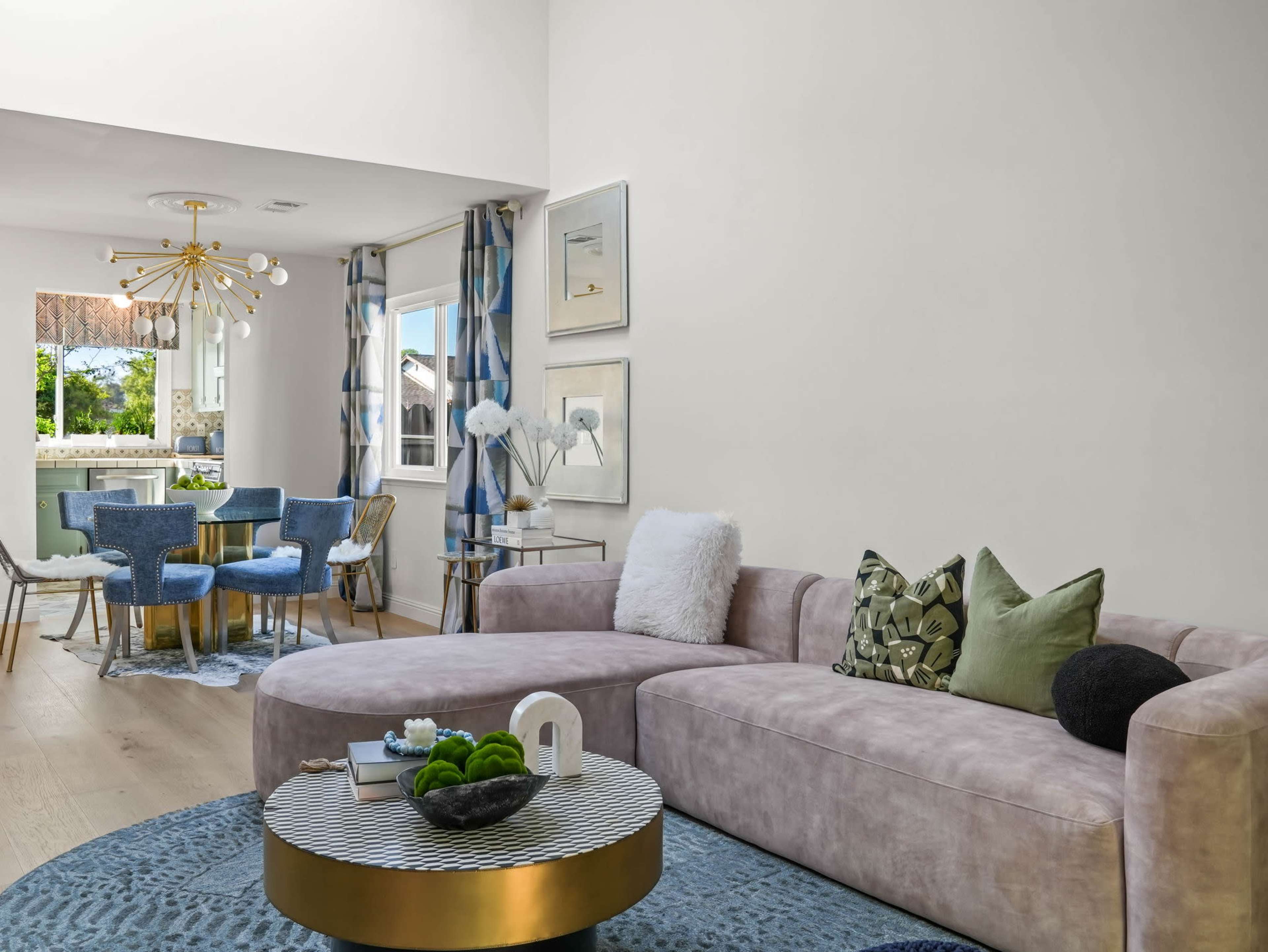 The image shows a modern living room with a pink sectional sofa, a round striped coffee table, and a dining area visible in the background.