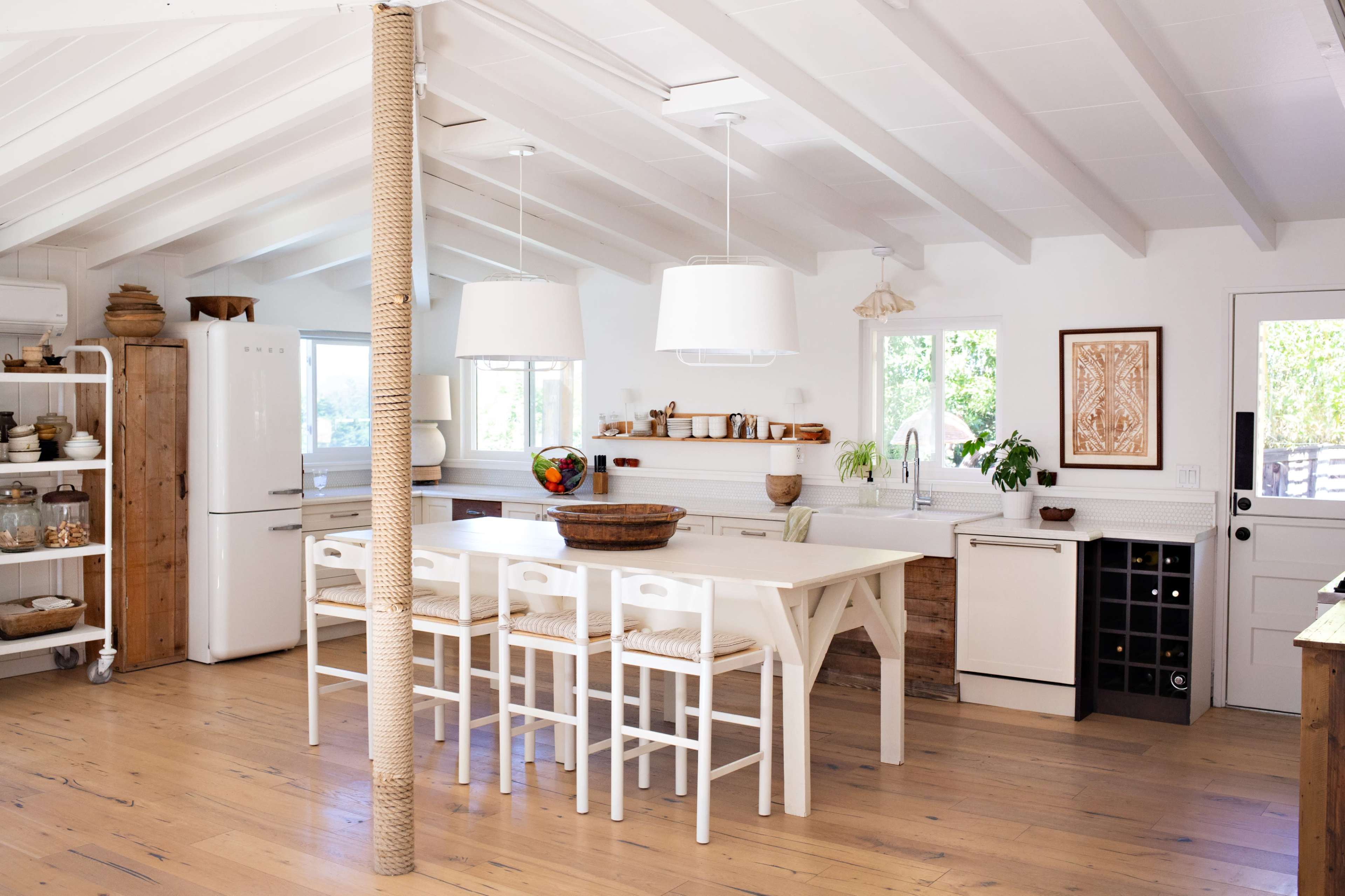 A bright kitchen with white cabinetry, wooden accents, a large island, and bar stools arranged around it.