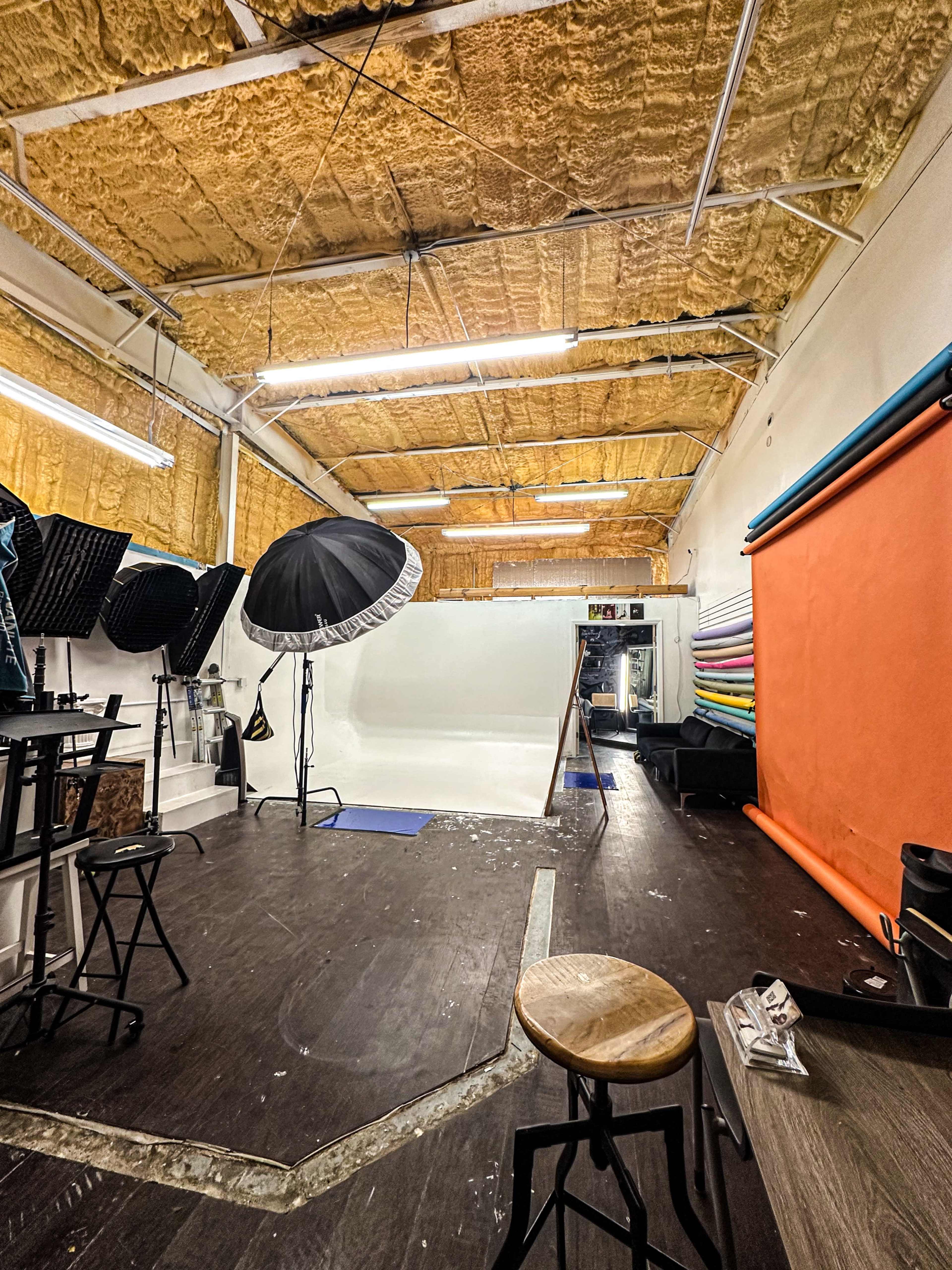 The image shows a photography studio with various lighting equipment, a seamless backdrop, and a wooden floor.
