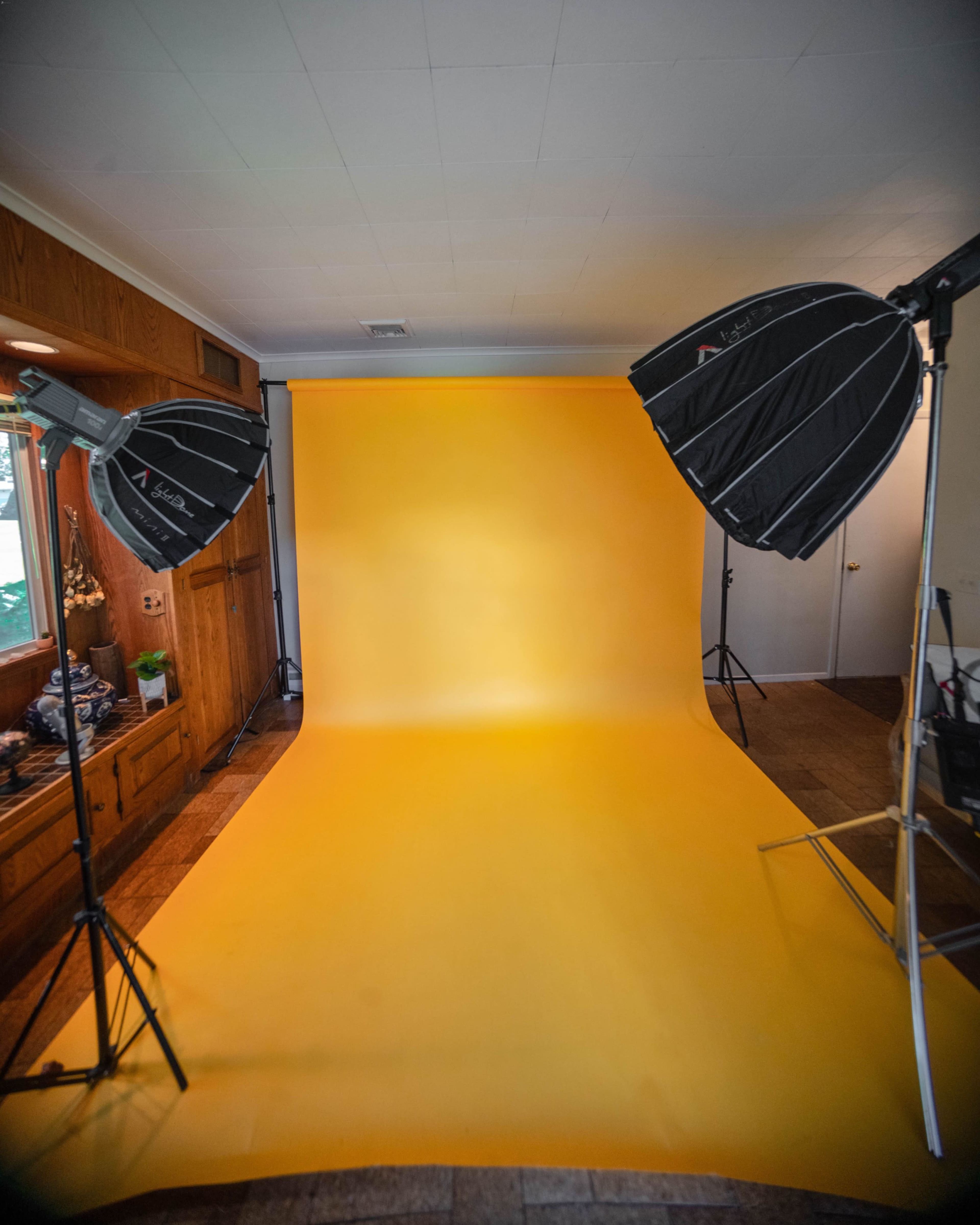 A photography studio setup with a yellow backdrop and two softbox lights positioned on either side.
