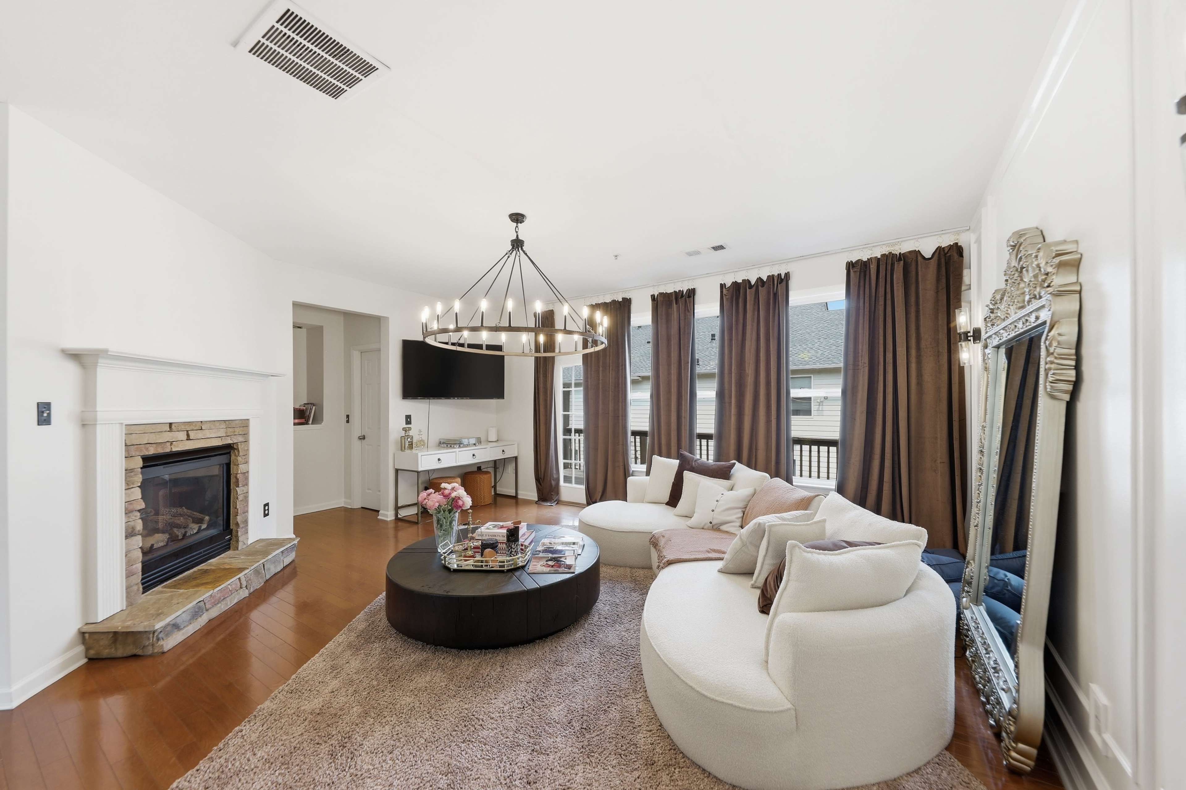 The living room features a circular coffee table and a large sectional sofa, with a fireplace and large windows draped in brown curtains.