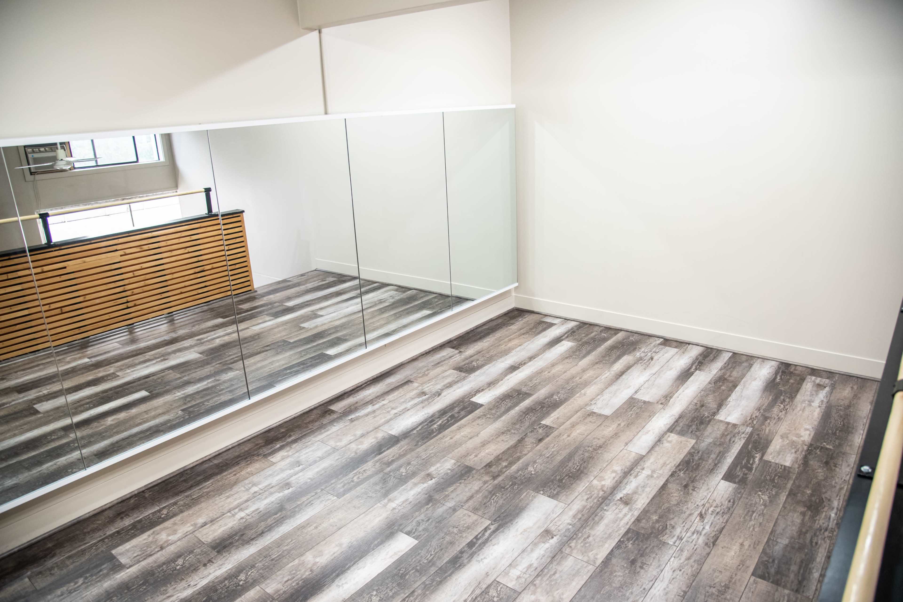 A spacious, mirrored room with wooden flooring and a wooden accent wall.