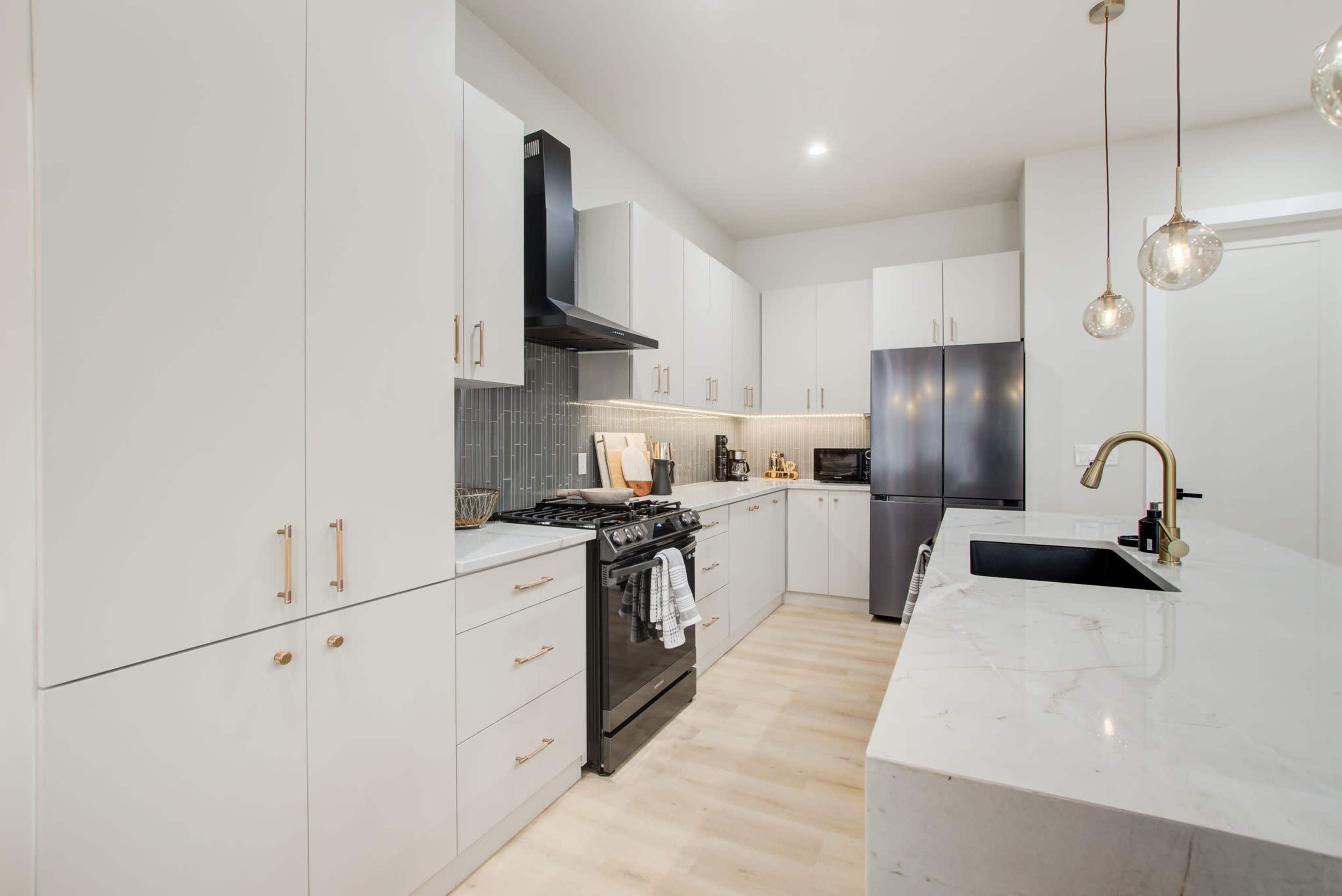 A modern kitchen features white cabinetry, a black stove, and a marble countertop with pendant lights overhead.