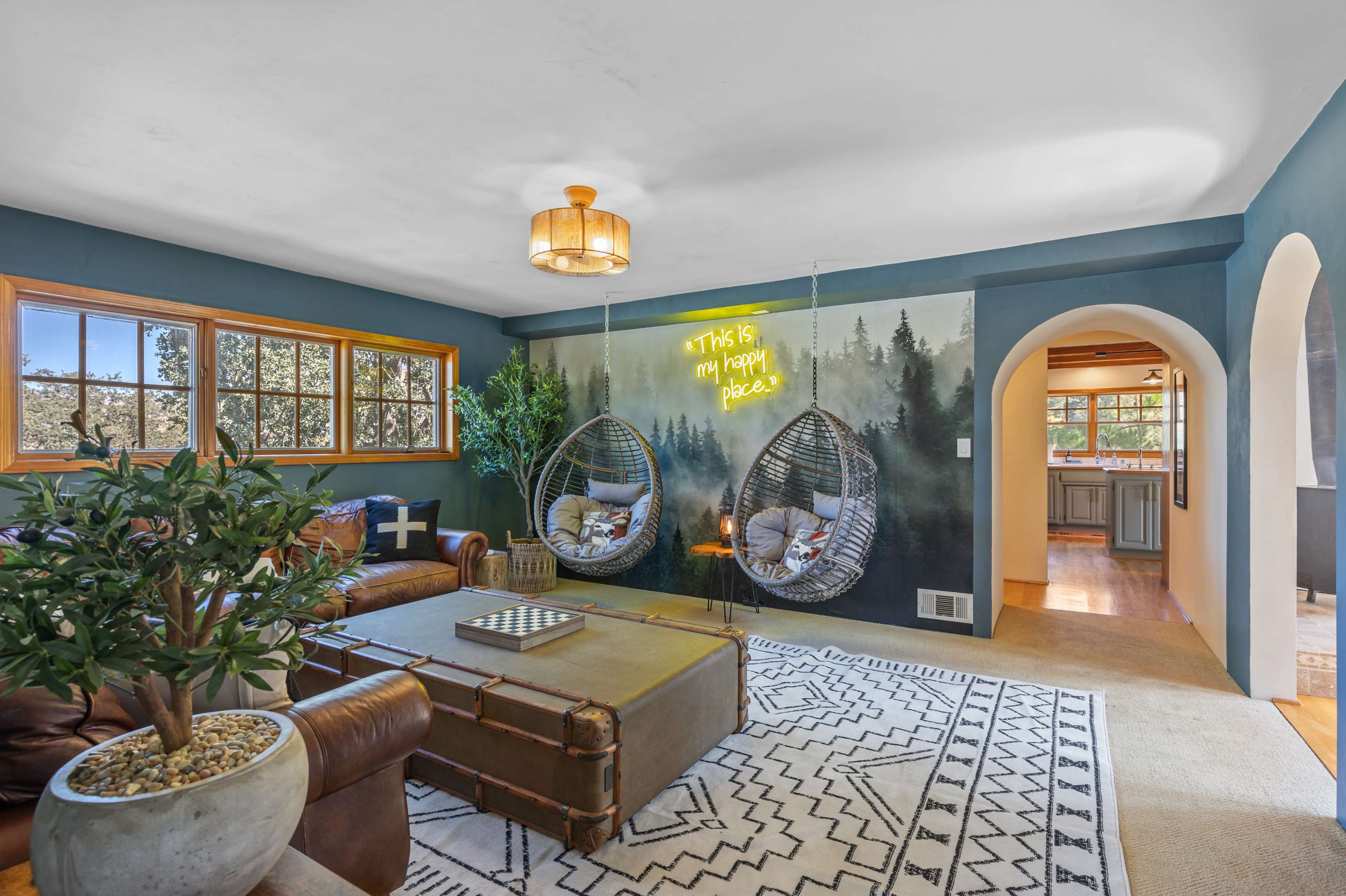 The living room features a cozy layout with a green accent wall, two hanging chairs, and a mural of a forest.