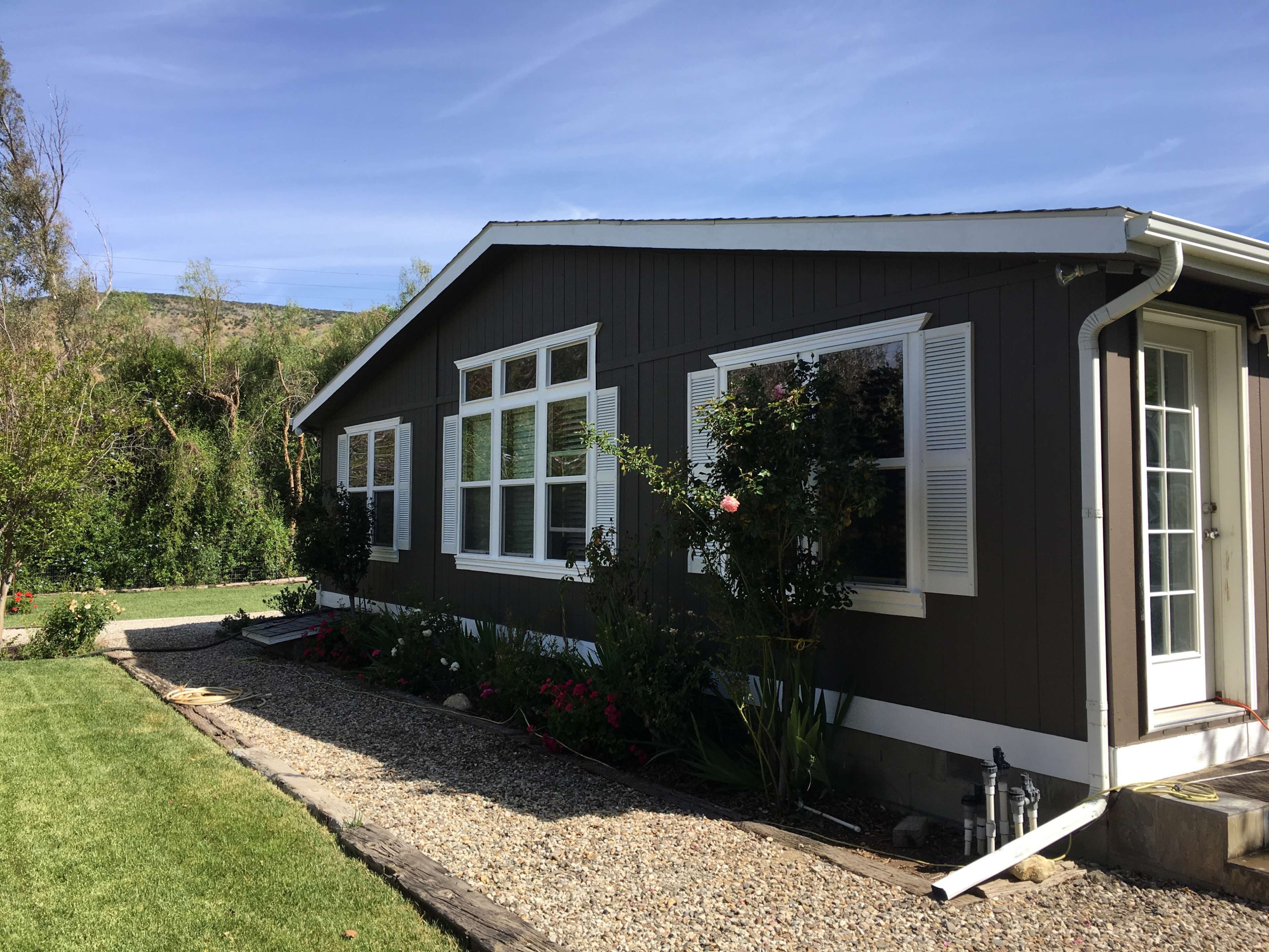 A side view of a dark-colored house with multiple windows, surrounded by a well-maintained garden and a gravel pathway.