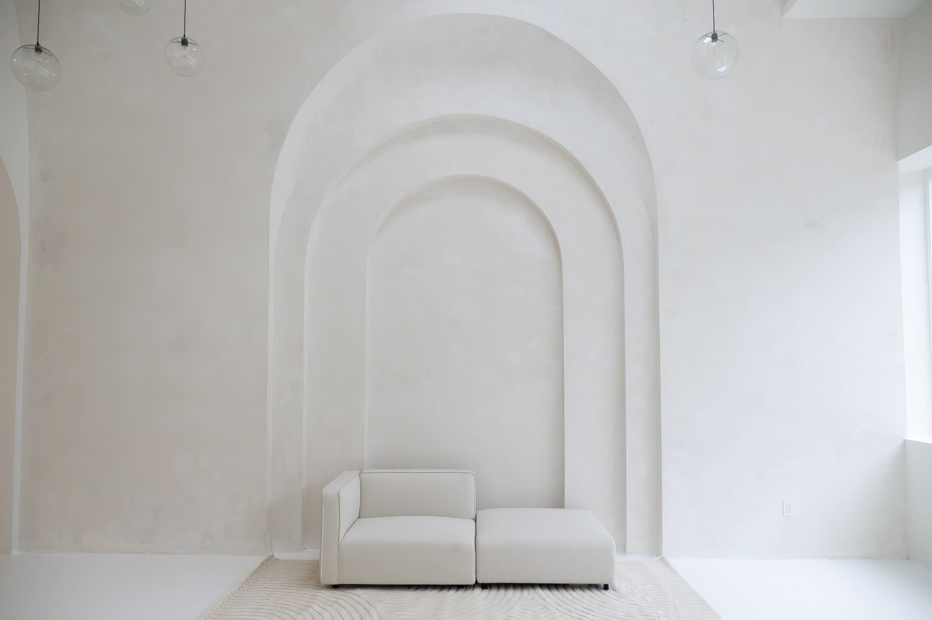 A minimalist room with white walls, an arched alcove, and a light-colored sofa positioned on a textured rug.