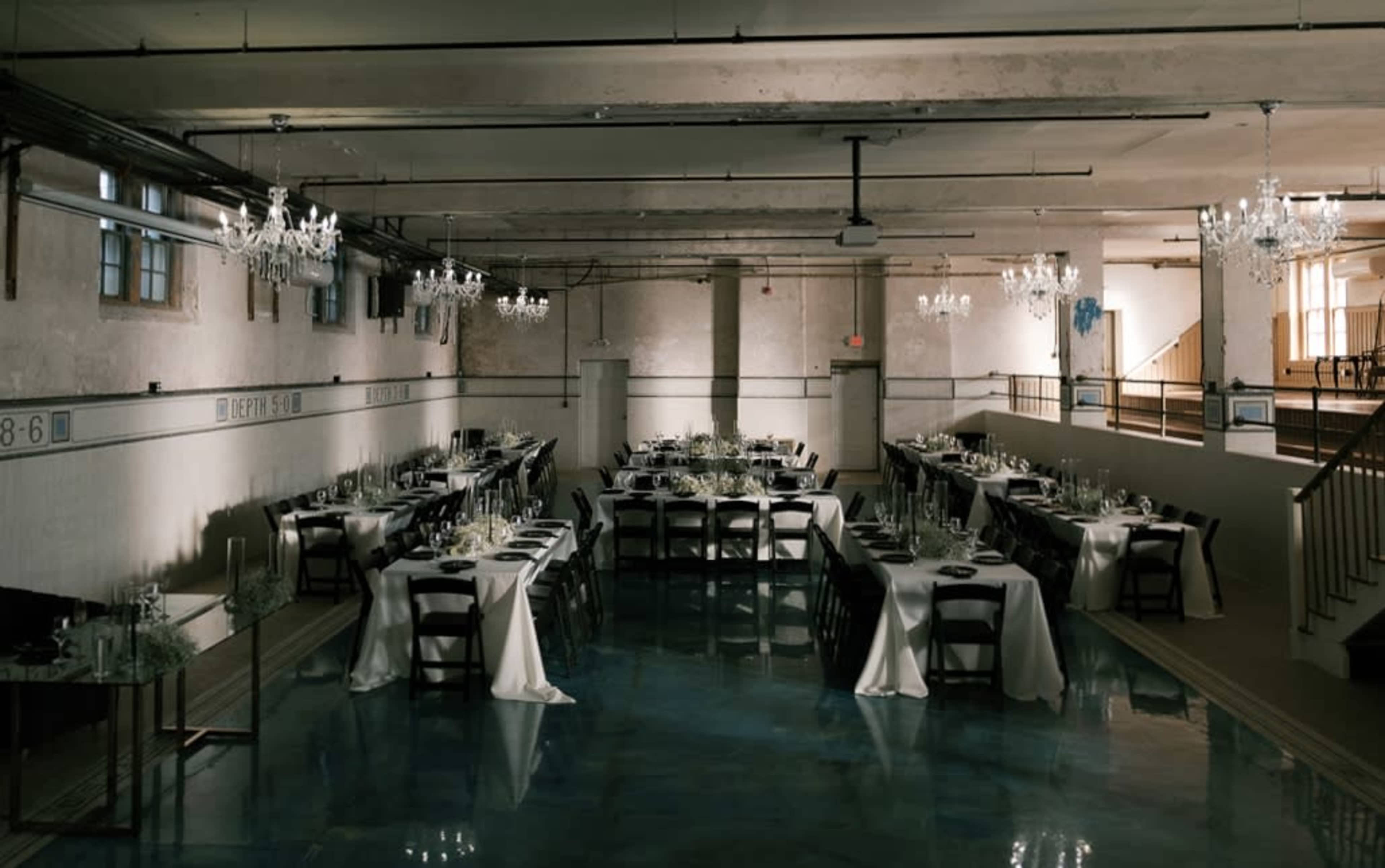 The image shows an elegantly arranged banquet hall with long tables set for a formal dinner, illuminated by chandeliers and featuring a polished floor.