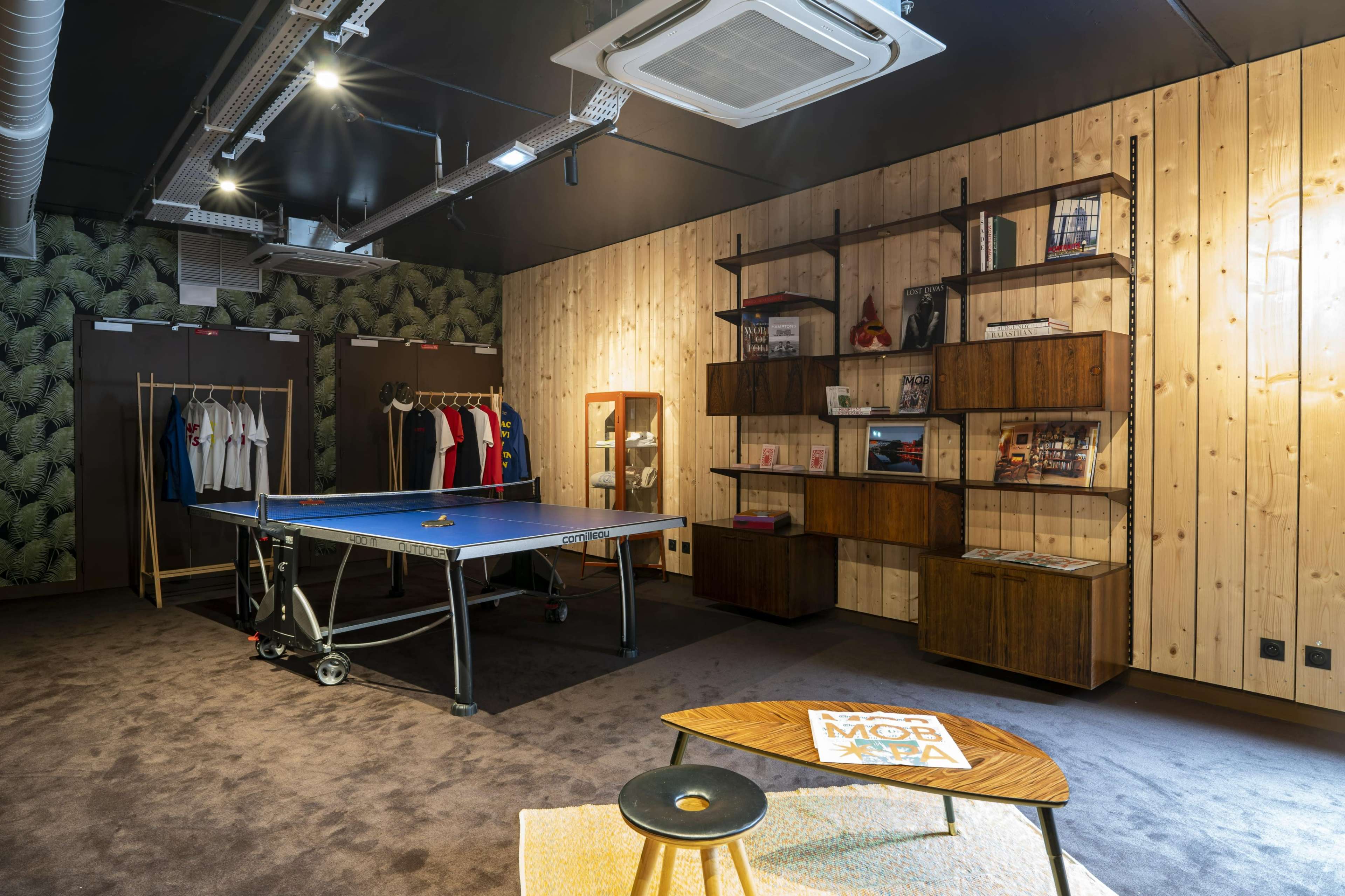 A modern interior space featuring a ping pong table, a wooden wall with shelving units, and a collection of clothing displayed on hangers.