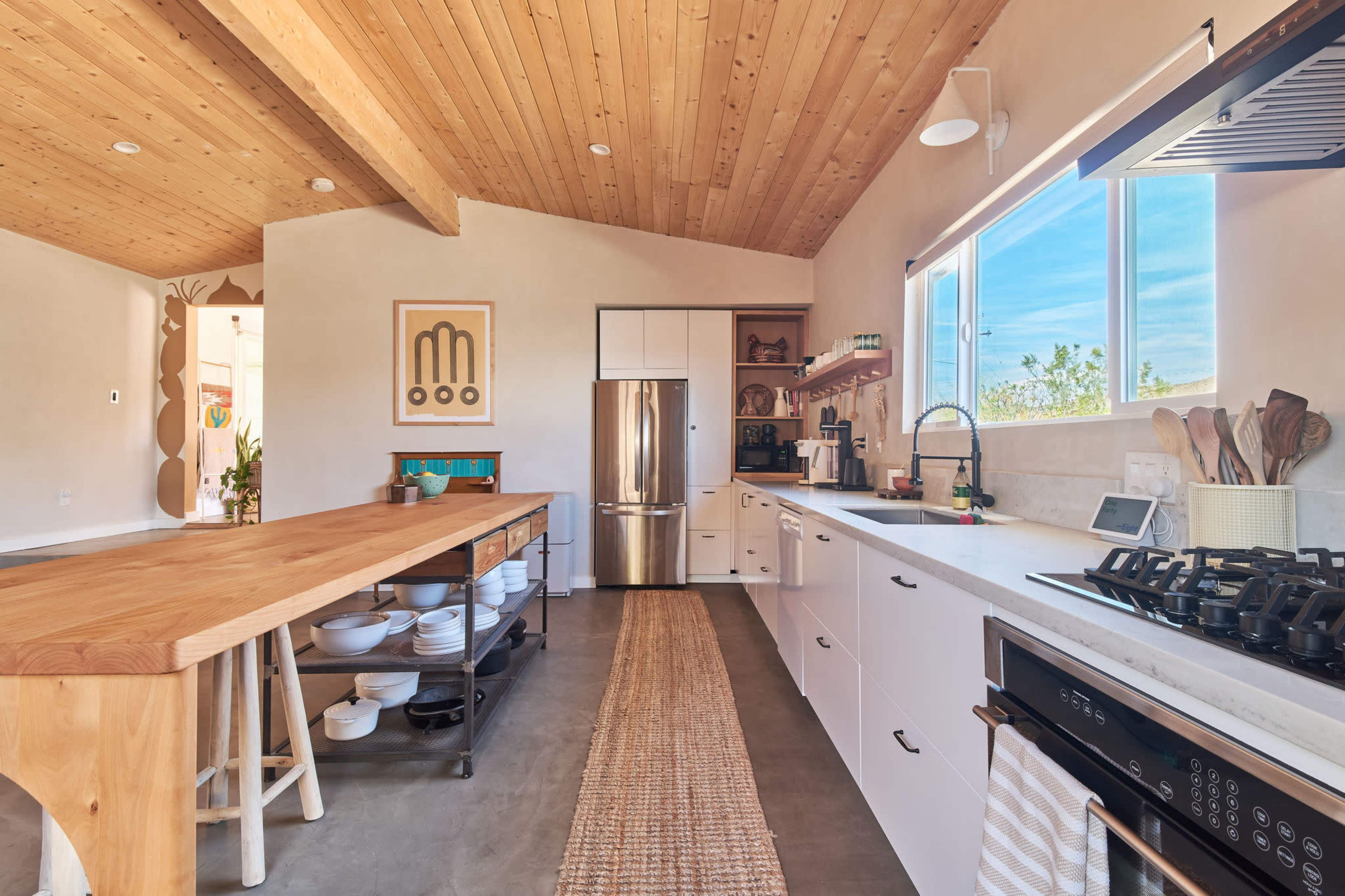 A modern kitchen featuring wooden beams, a large wooden island, and white cabinetry with stainless steel appliances.