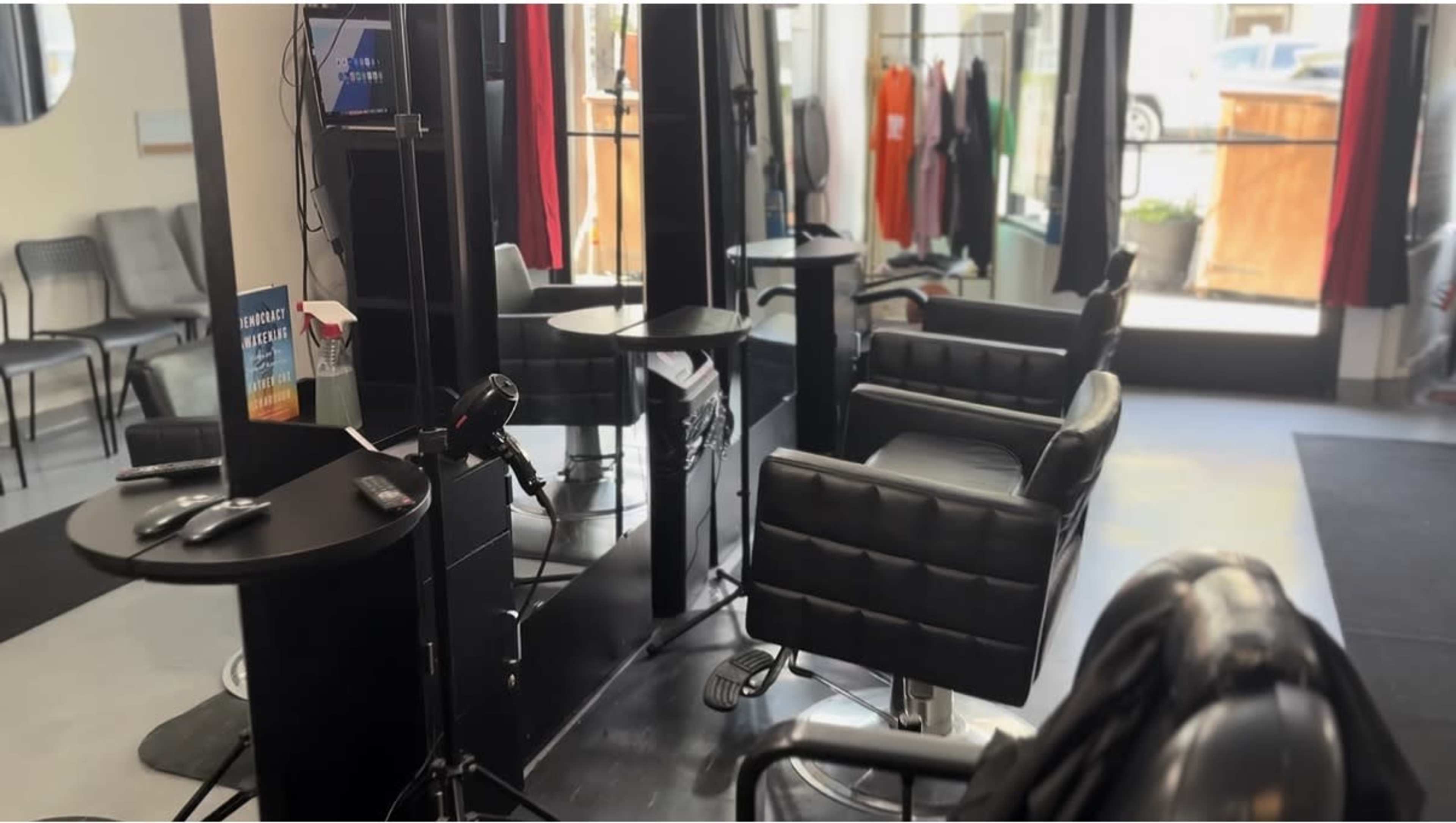 The image shows the interior of a hair salon with black styling chairs, mirrors, and a reception area.