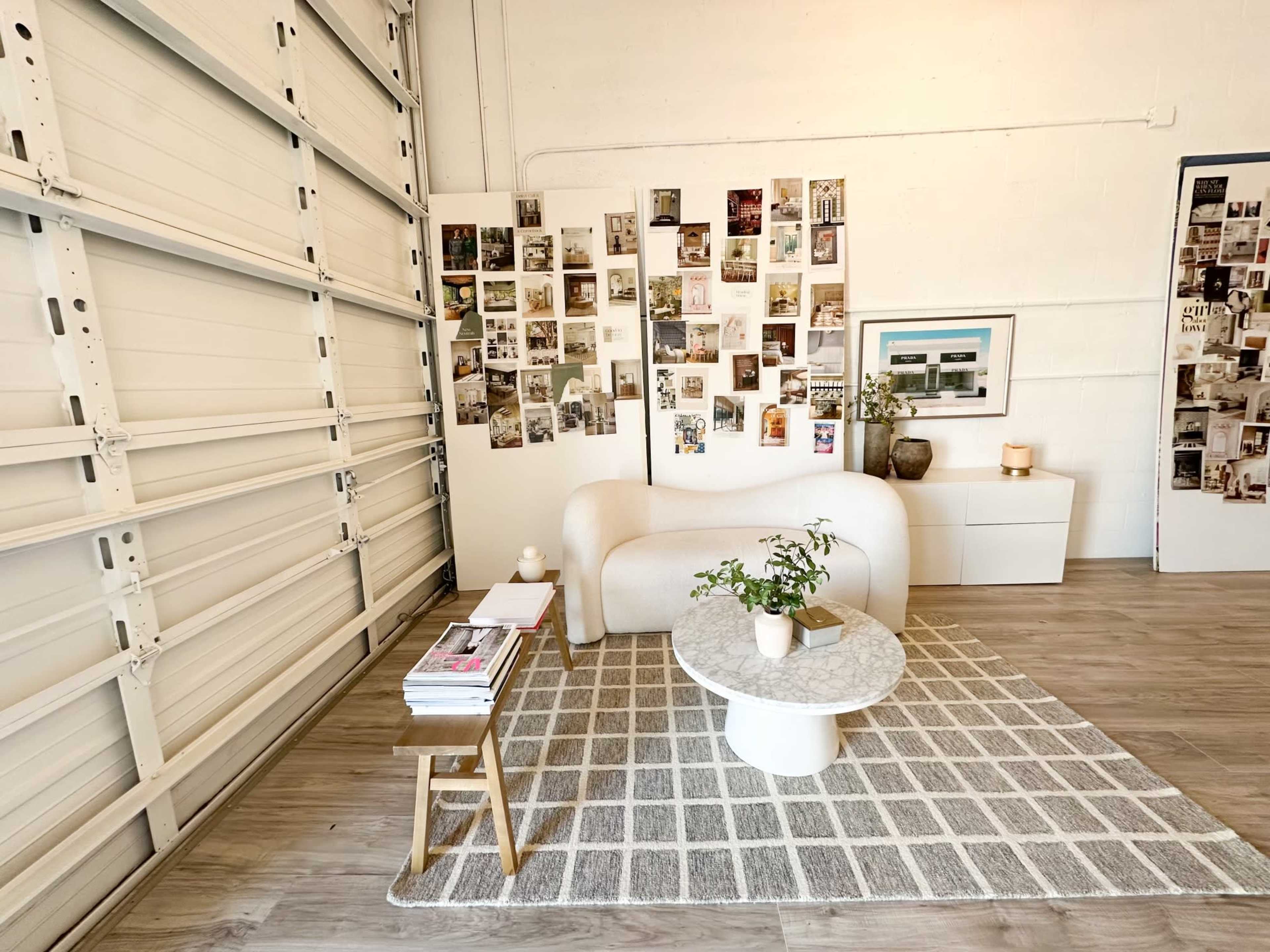 A modern living space featuring a white curved sofa, a round coffee table, a patterned rug, and a wall adorned with a collage of photographs.
