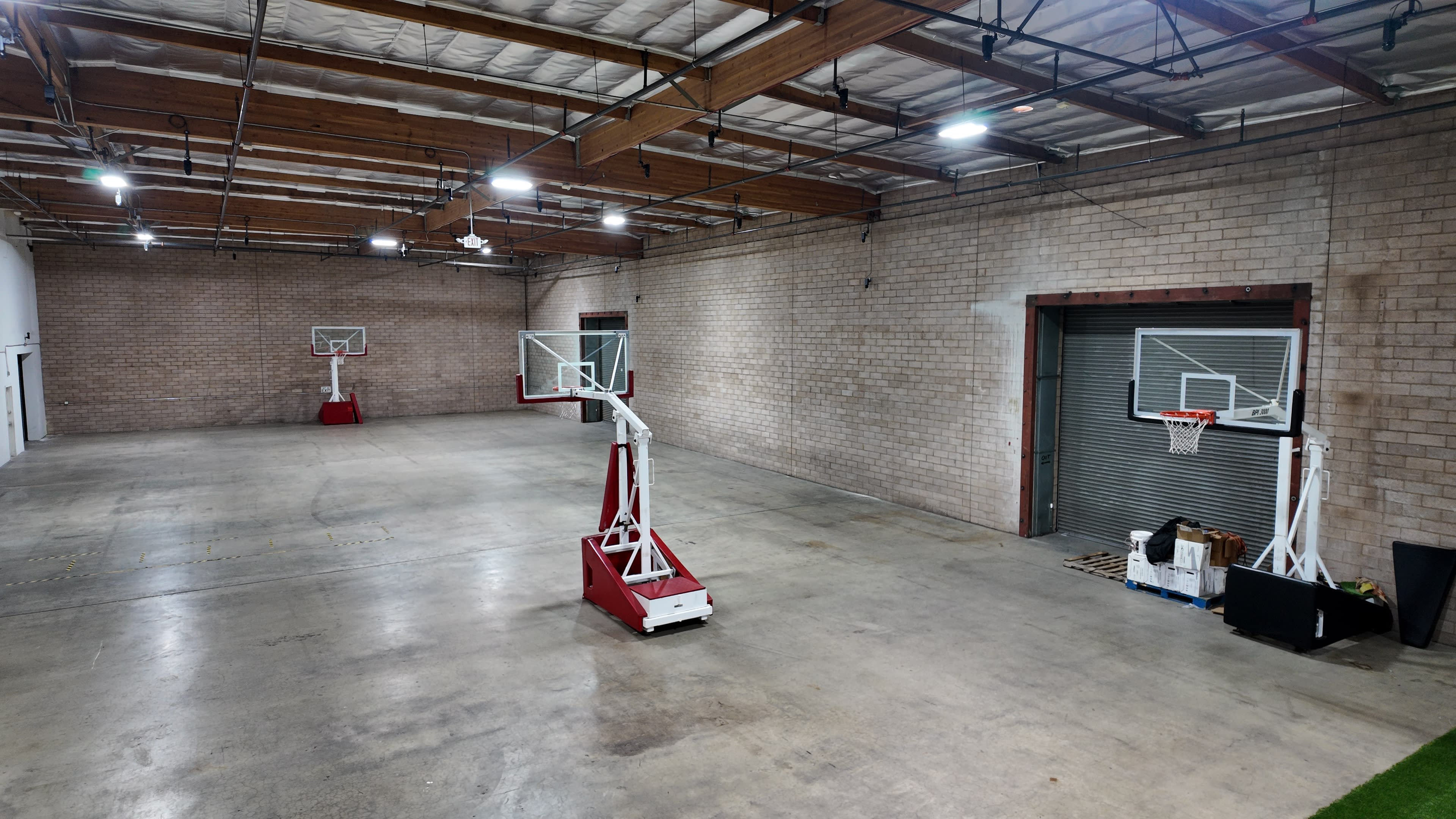 The image shows a spacious indoor facility with two basketball hoops set up on opposite ends and a concrete floor under bright overhead lights.