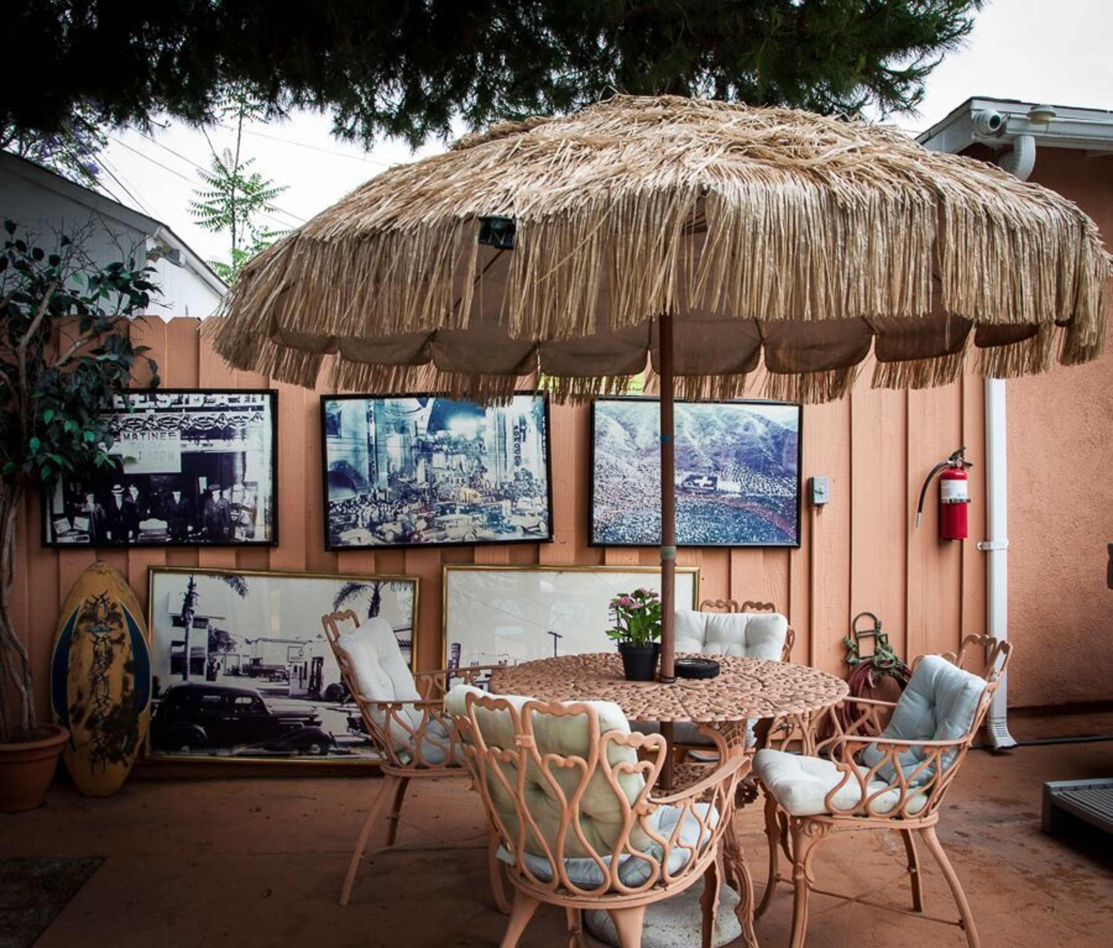 A patio area features a round table with four chairs beneath a thatched umbrella, bordered by framed photographs on a peach-colored wall.