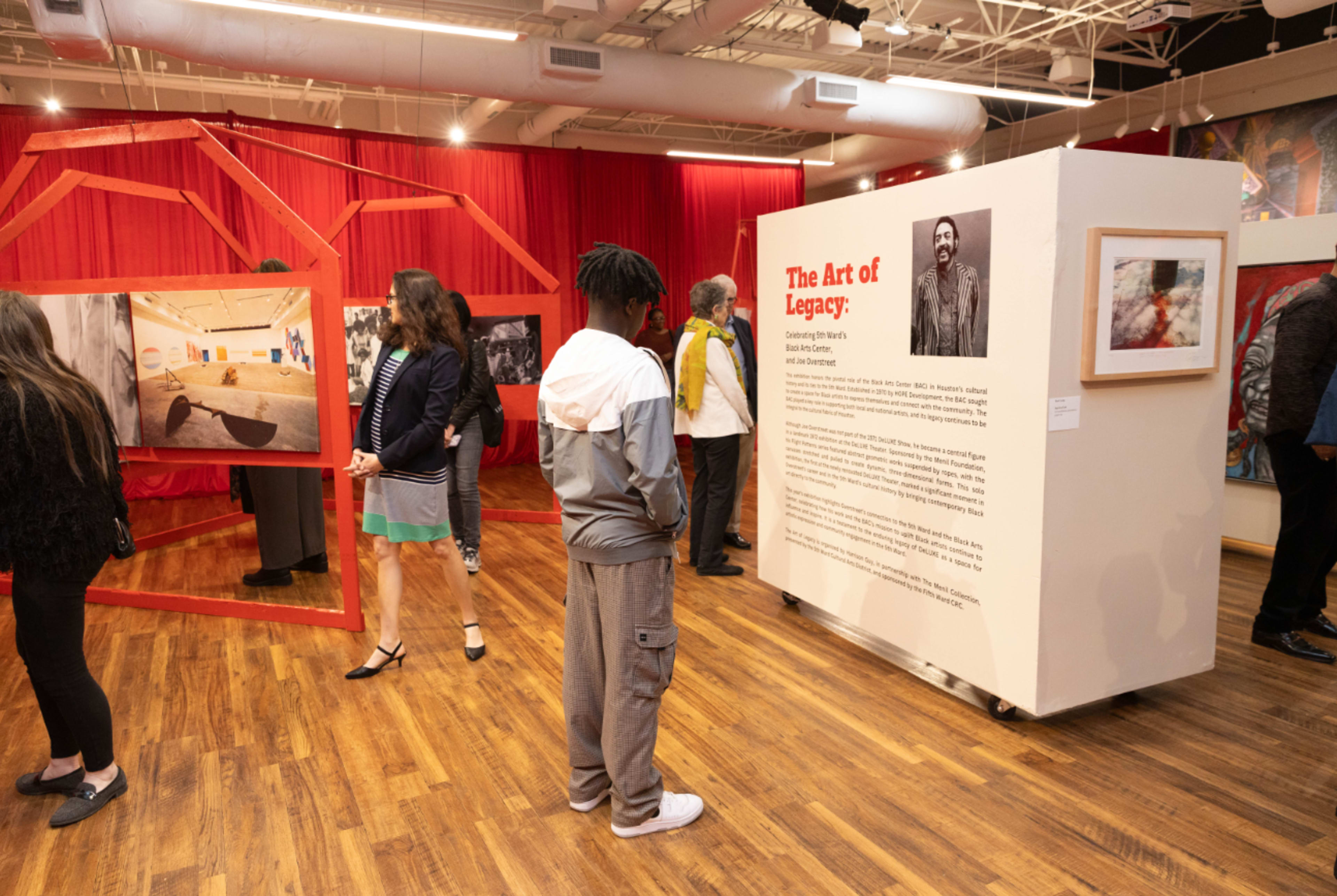 A group of visitors examines photographic art displays at an exhibition titled "The Art of Legacy" in a gallery.