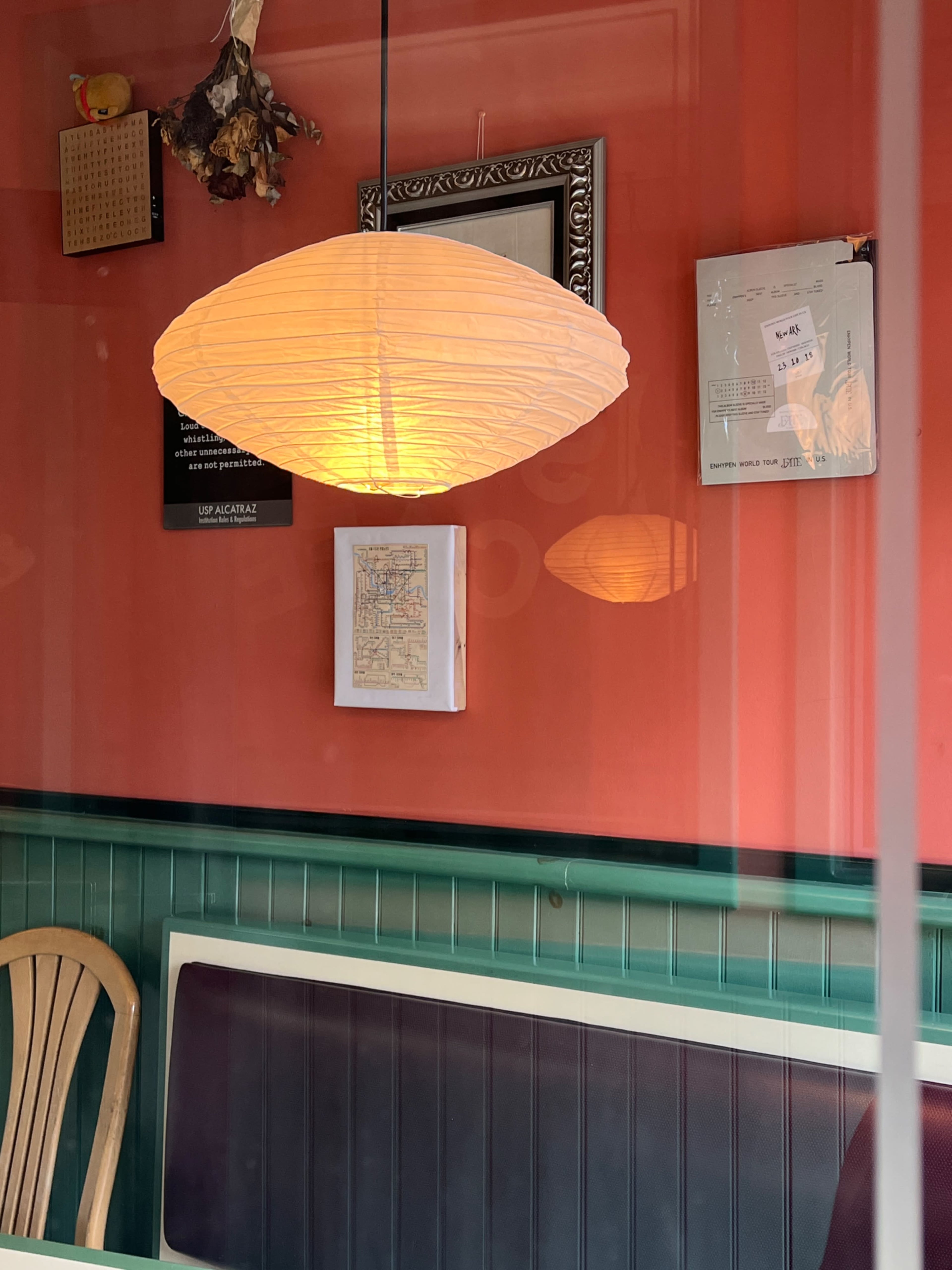 A hanging paper lantern illuminates a wall adorned with framed art and a map in a cafe setting.