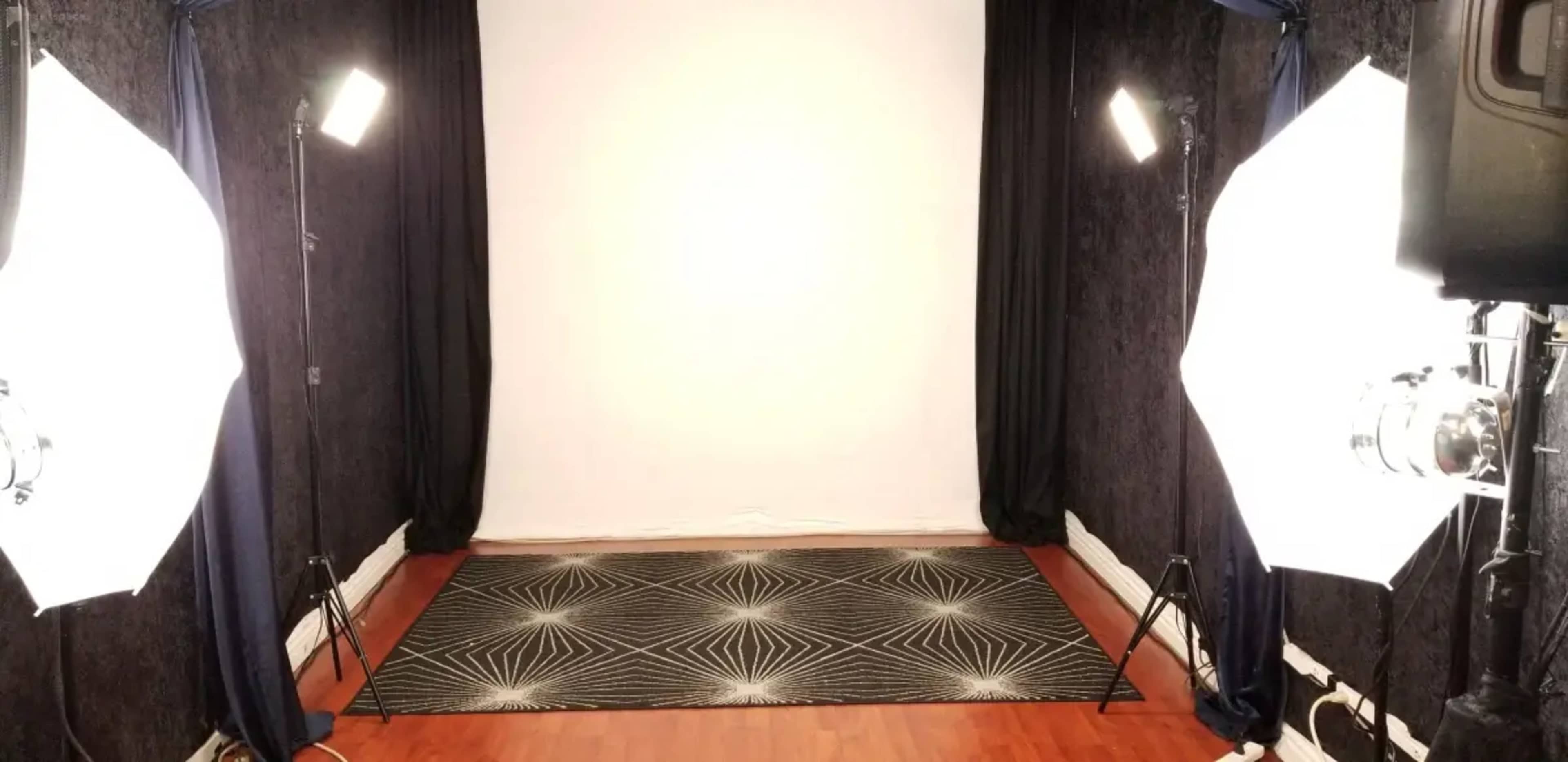 The image shows a photography studio setup with white backdrop, black curtains, and bright lights positioned on either side.