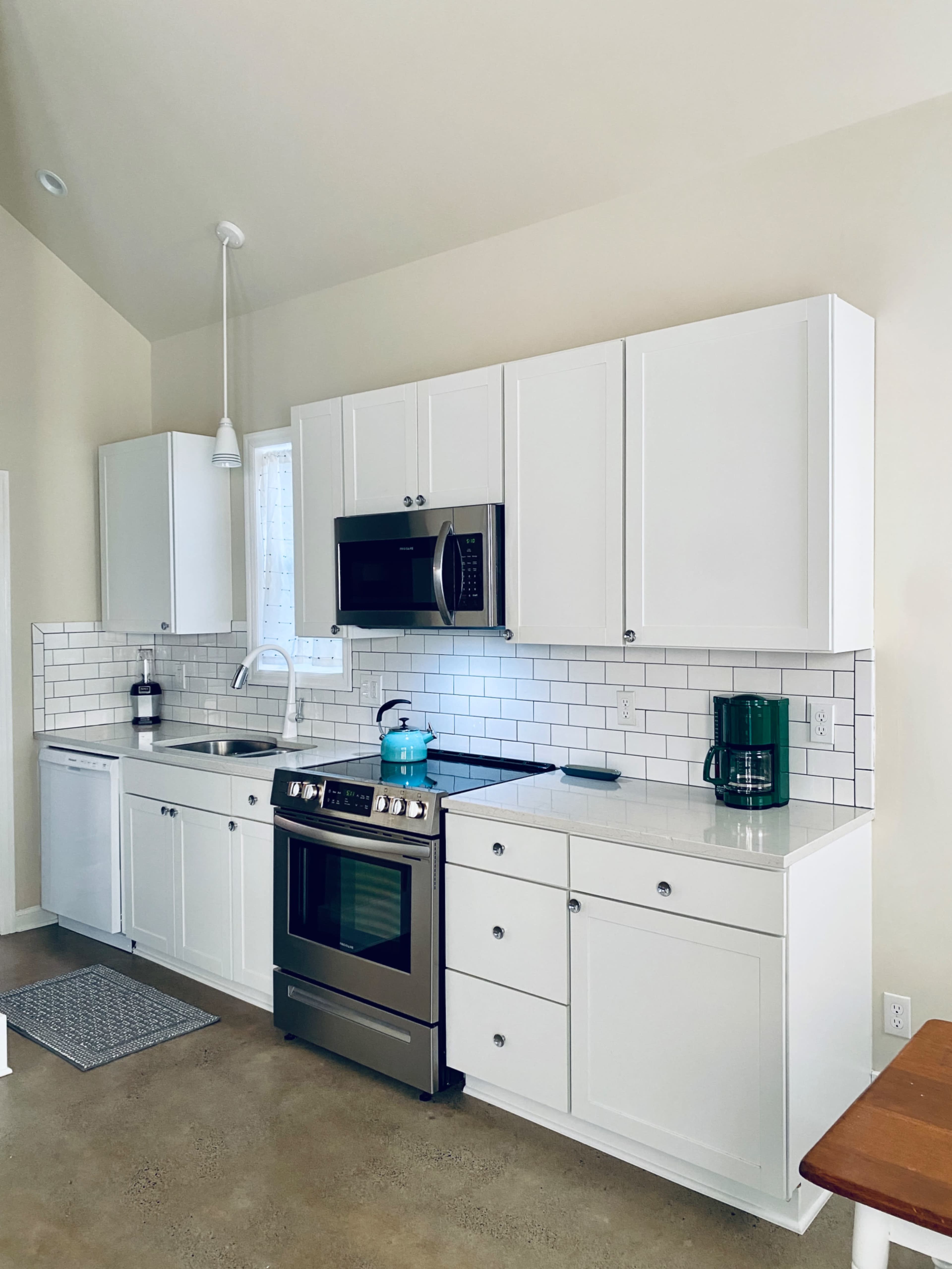 The image shows a modern kitchen featuring white cabinetry, stainless steel appliances, and a tiled backsplash.