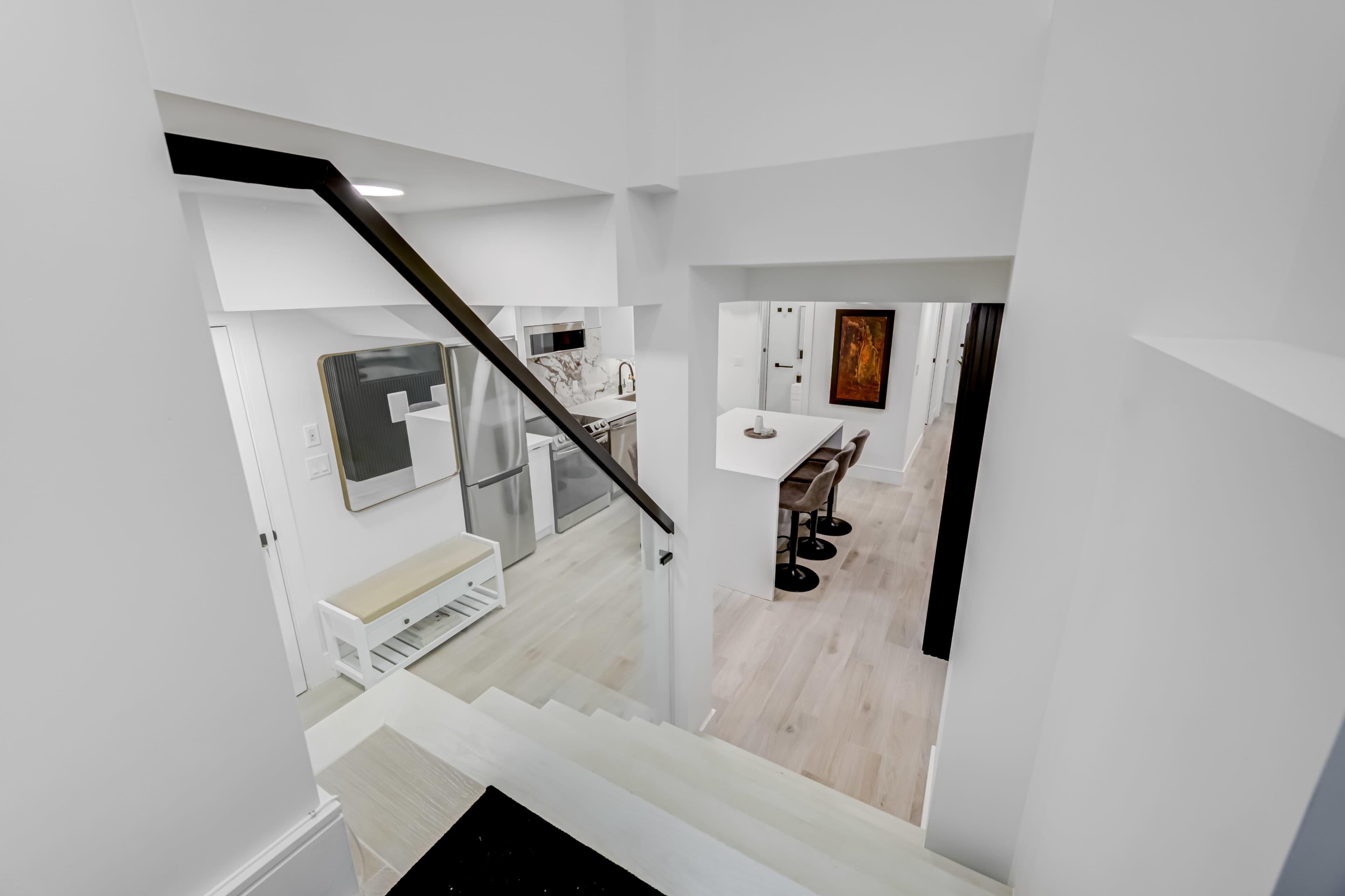 A staircase leads down to a bright, modern open space encompassing a kitchen and dining area.