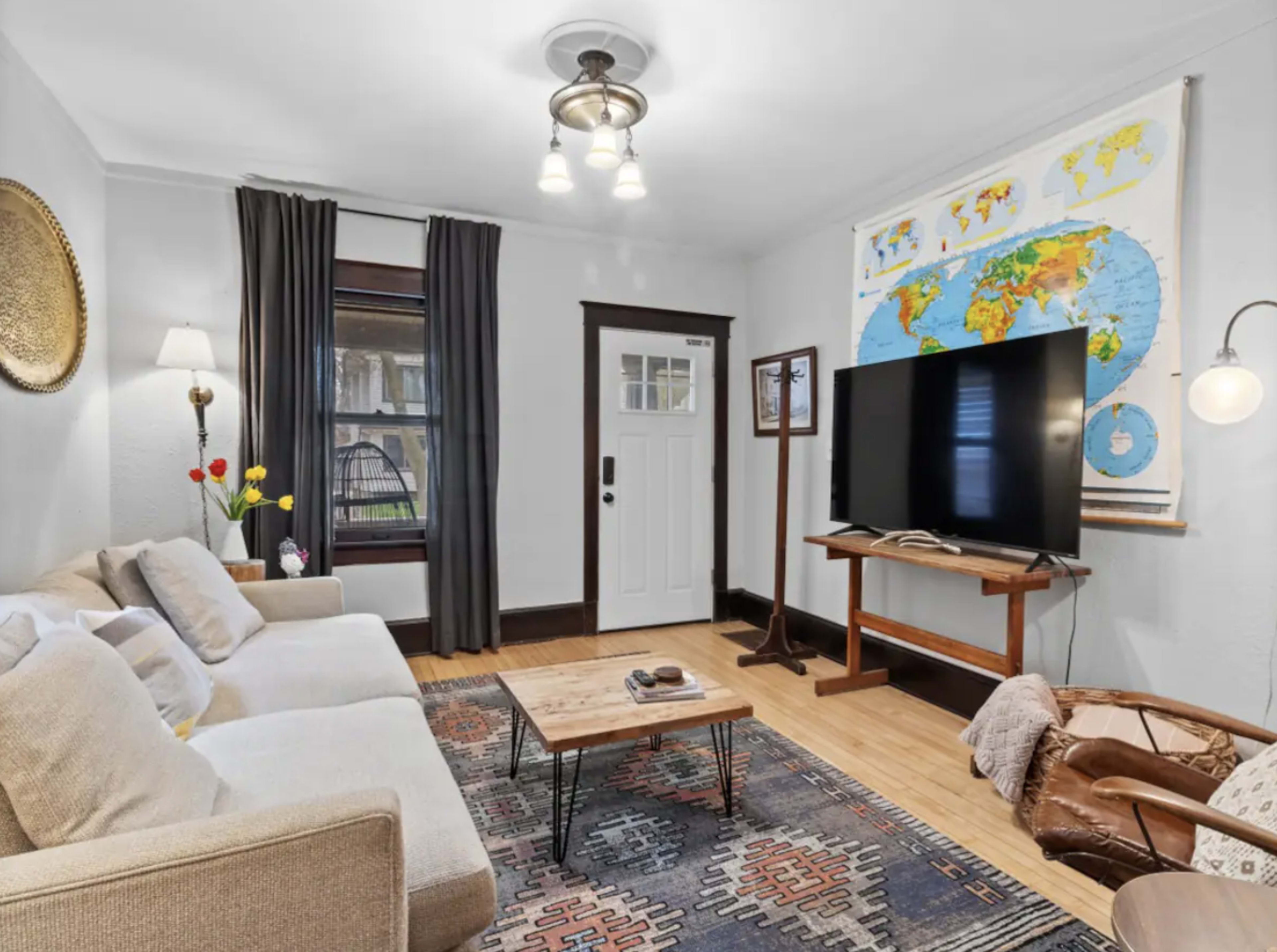 A living room features a neutral sofa, a wooden coffee table, a large TV on a stand, and a world map hanging on the wall.