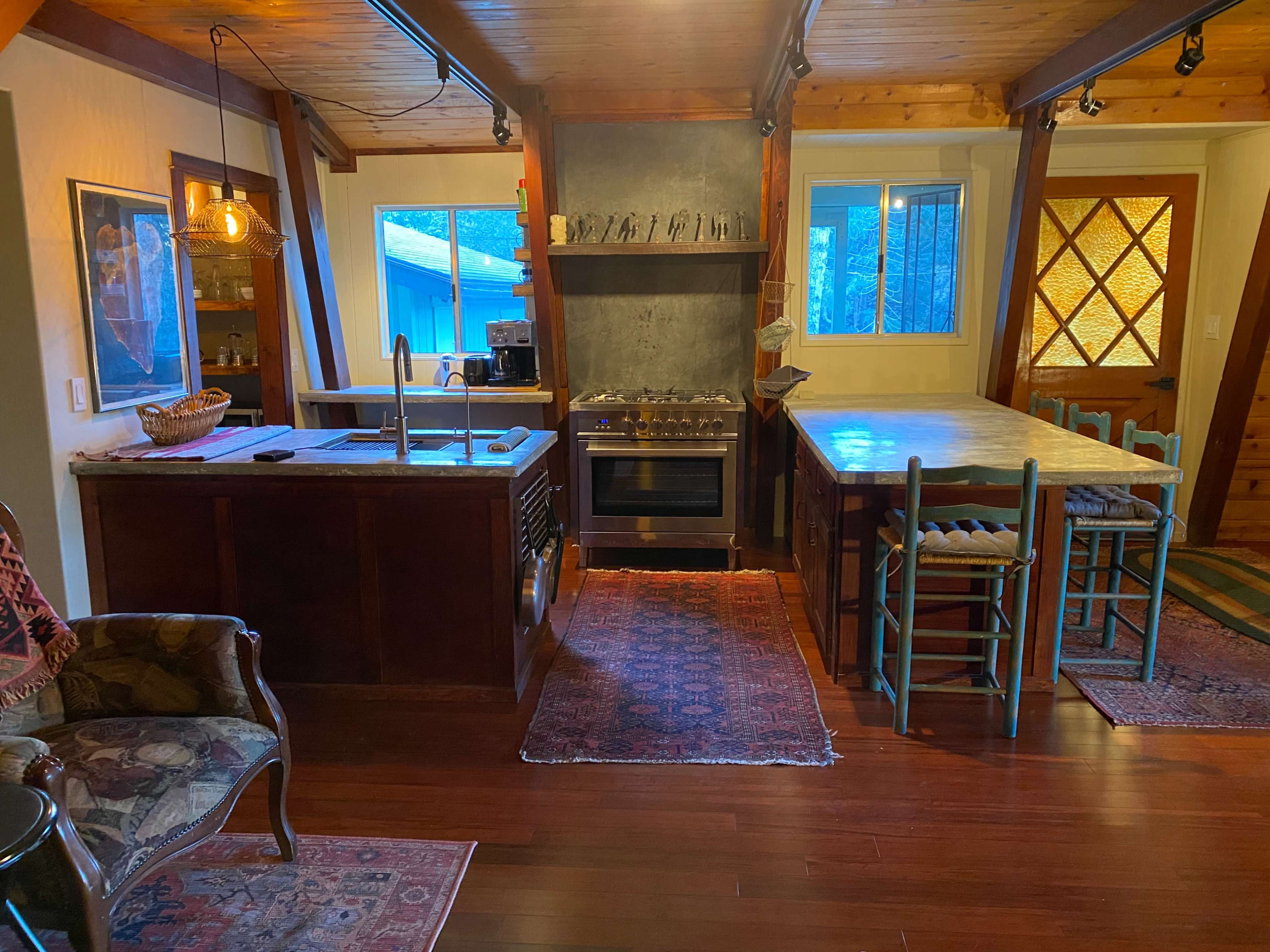 A kitchen area with wooden beams, a marble-topped island, a stove, and a dining table surrounded by chairs.