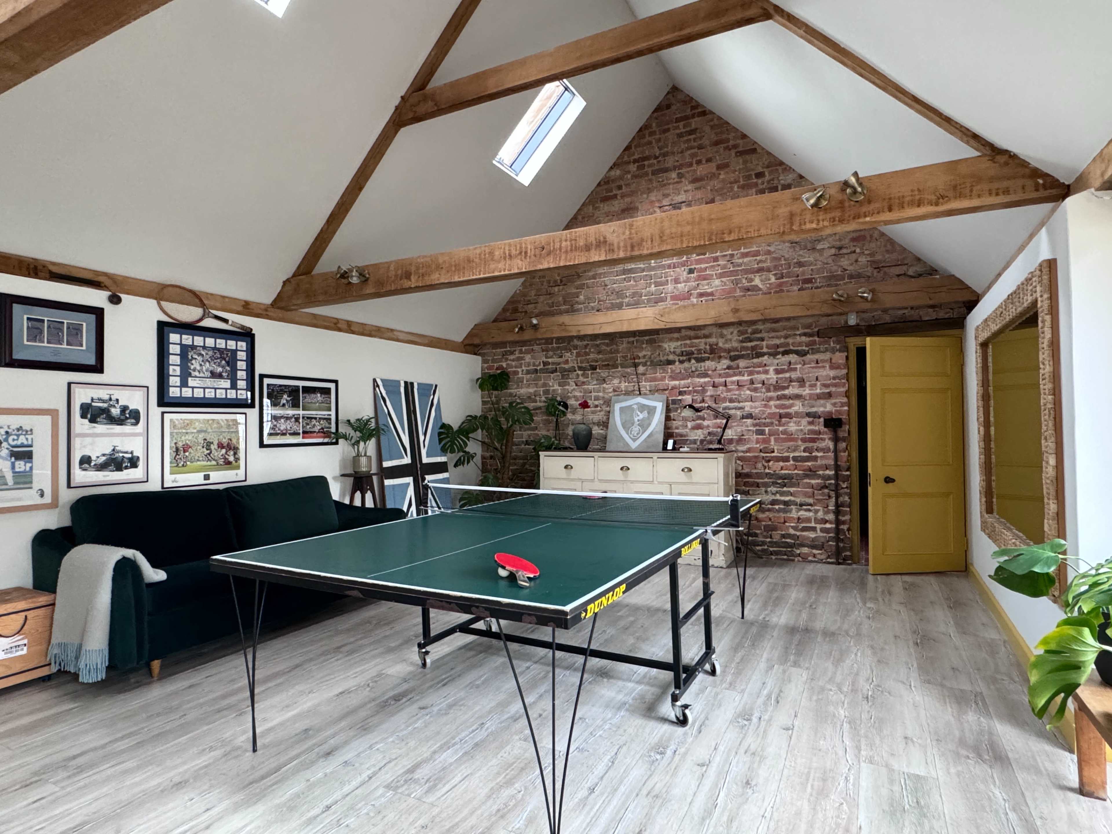 A game room featuring a ping pong table, exposed brick walls, wooden beams, and a green door.