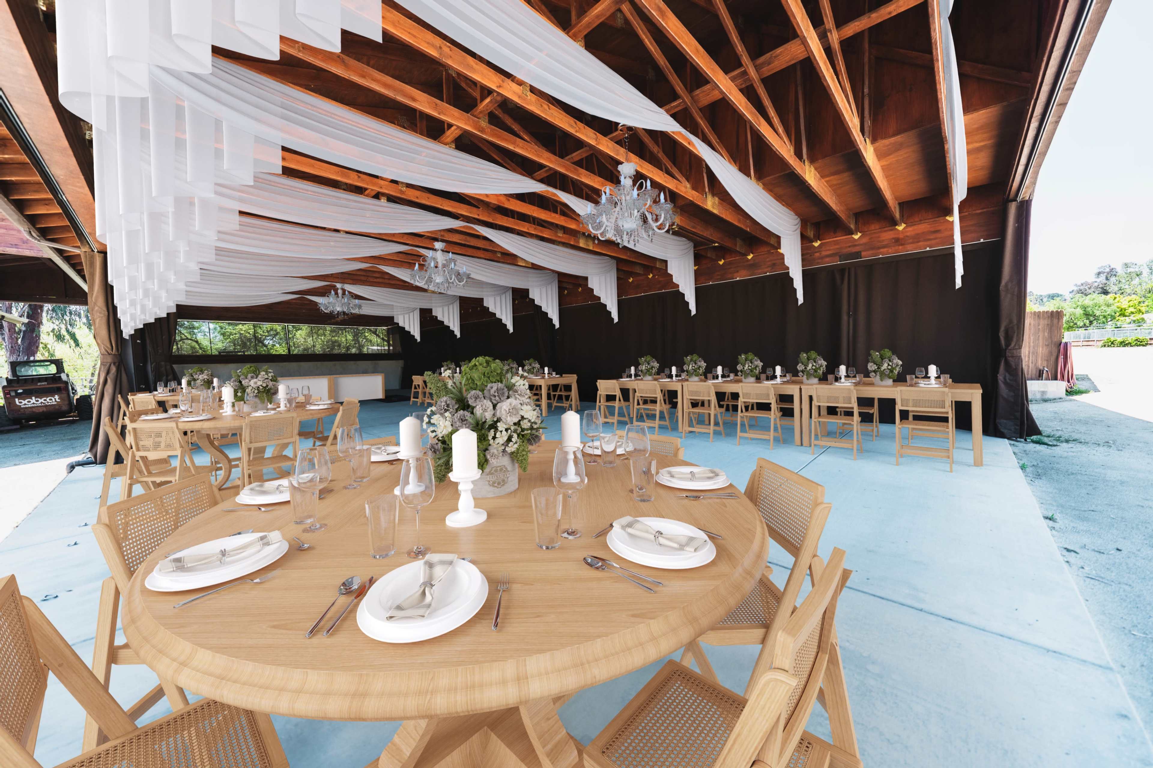 A spacious indoor dining area with wooden tables and chairs set for a meal, featuring elegant decor and draped fabric overhead.