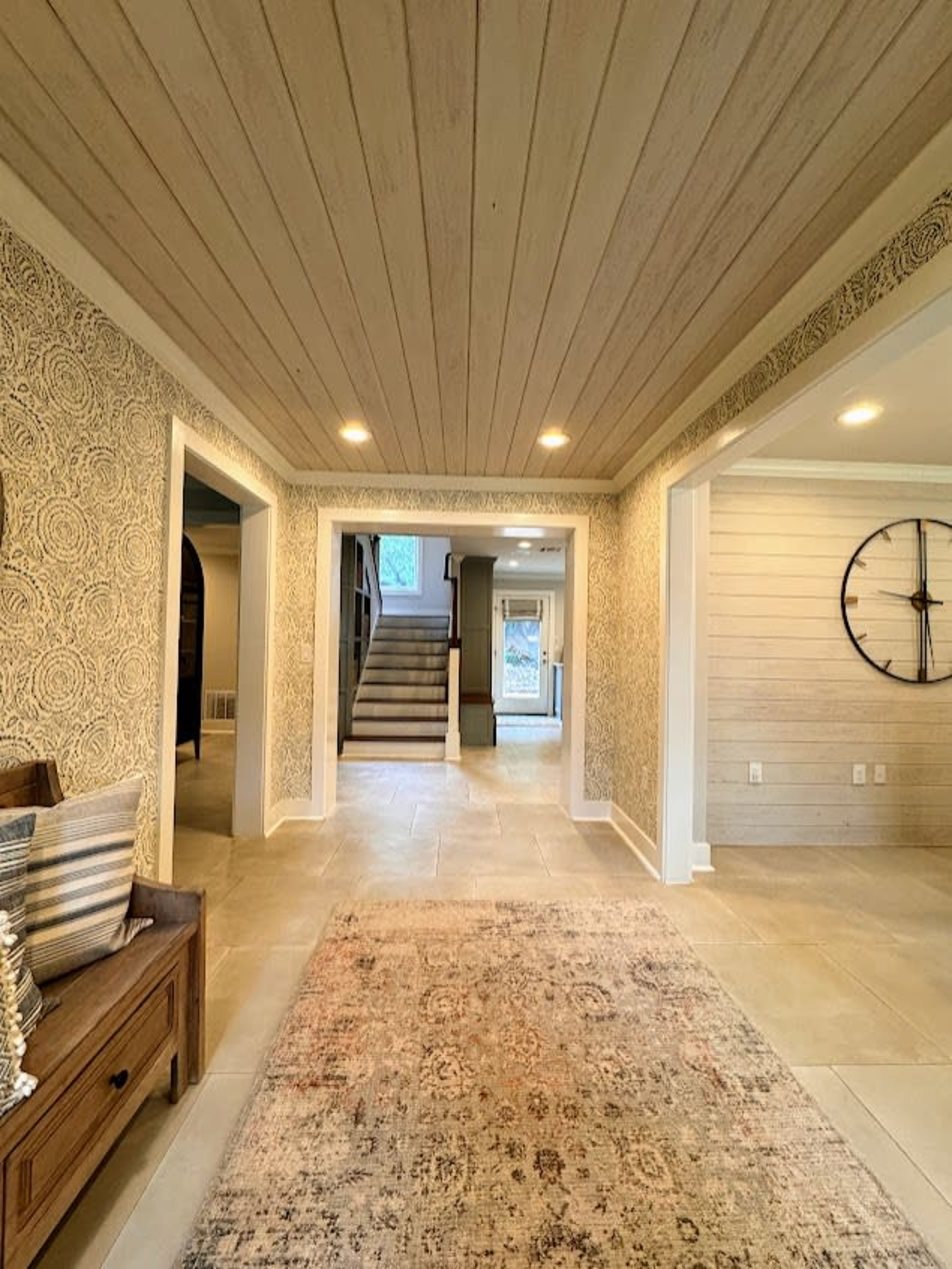 A spacious hallway with light-colored walls, a patterned rug on the floor, and a staircase leading to an upper level.