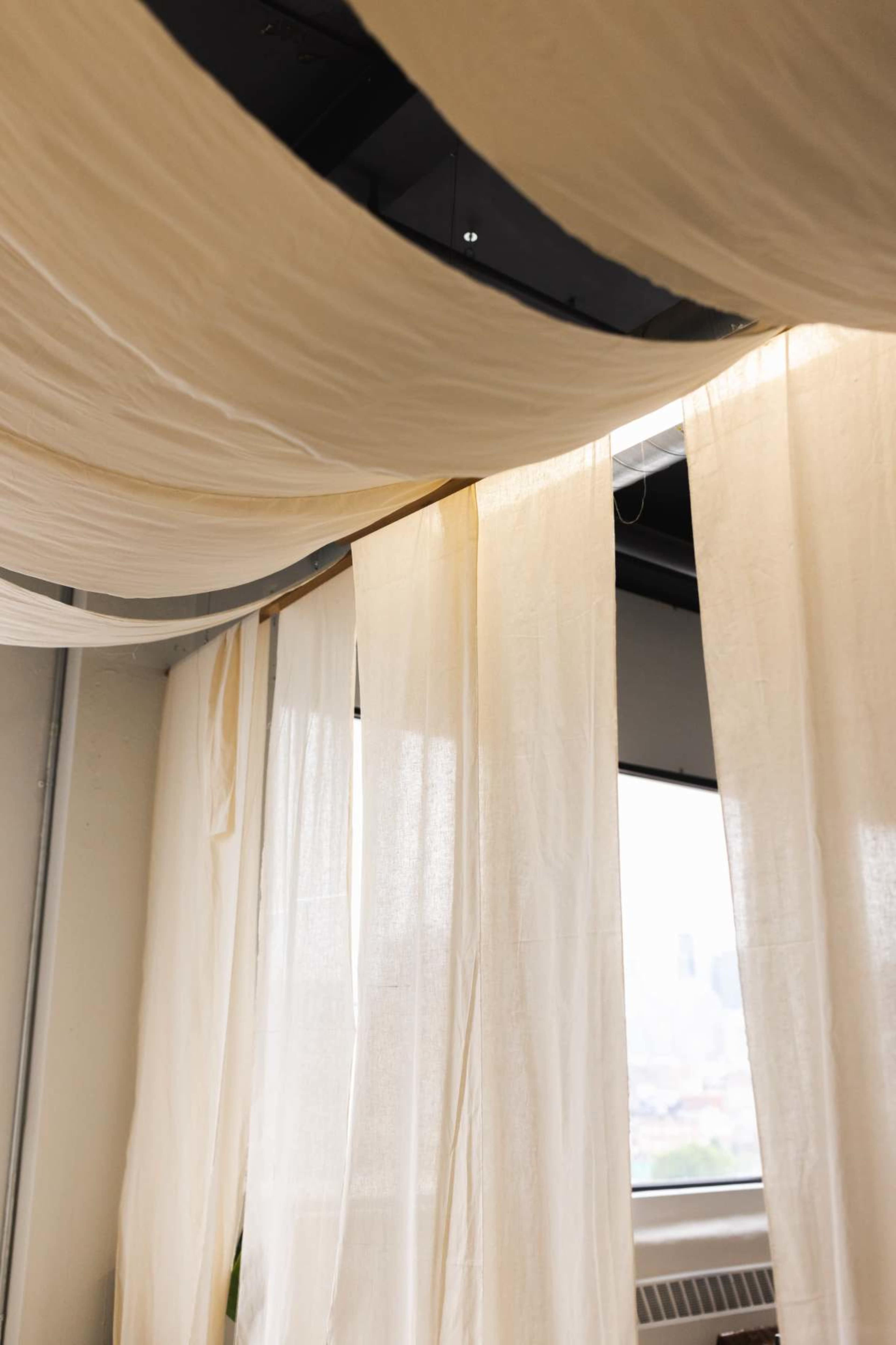 The image depicts flowing, cream-colored fabric draped from the ceiling in a room with a window in the background.