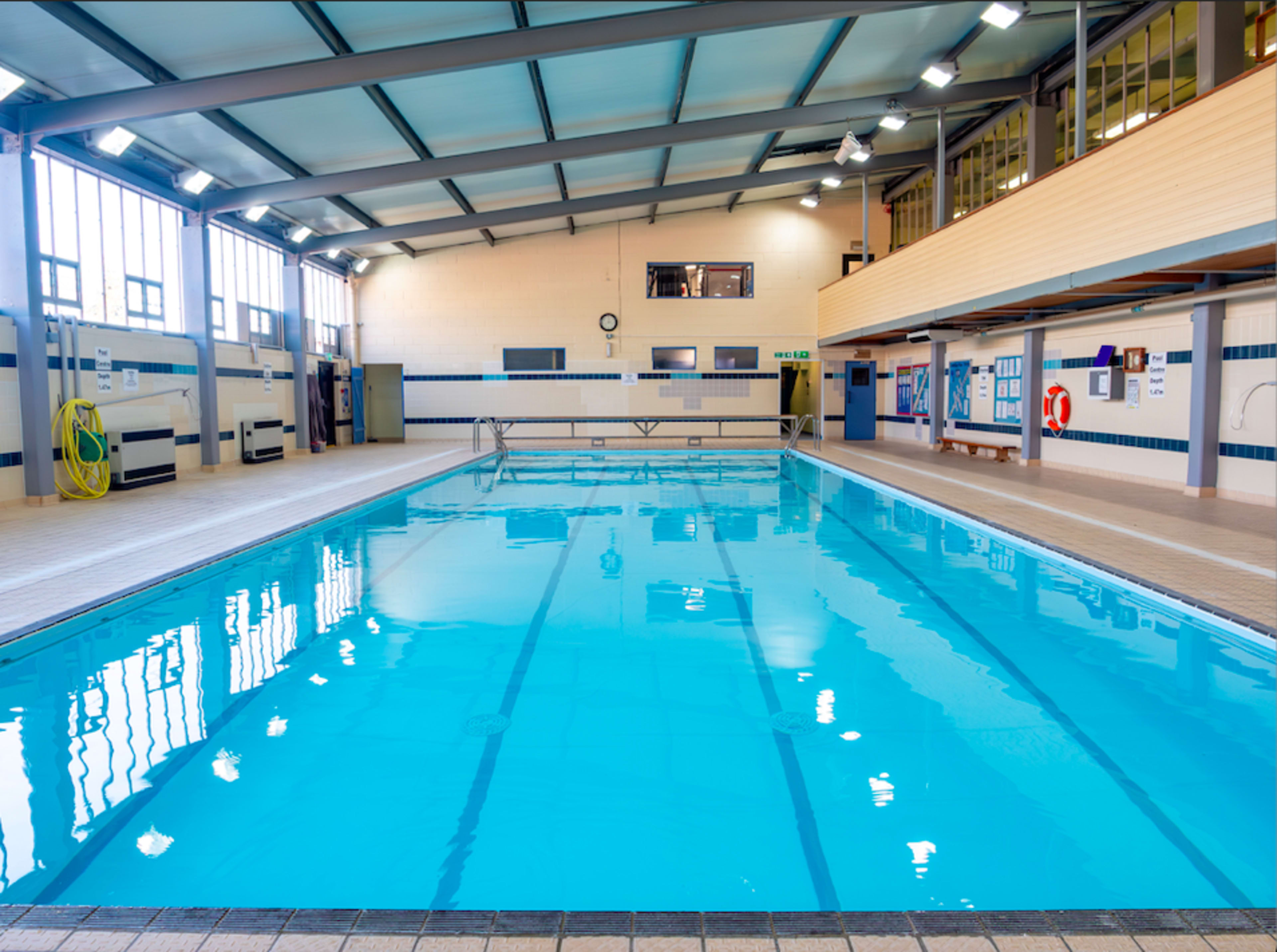 A well-lit indoor swimming pool with clear blue water and a wooden deck area.