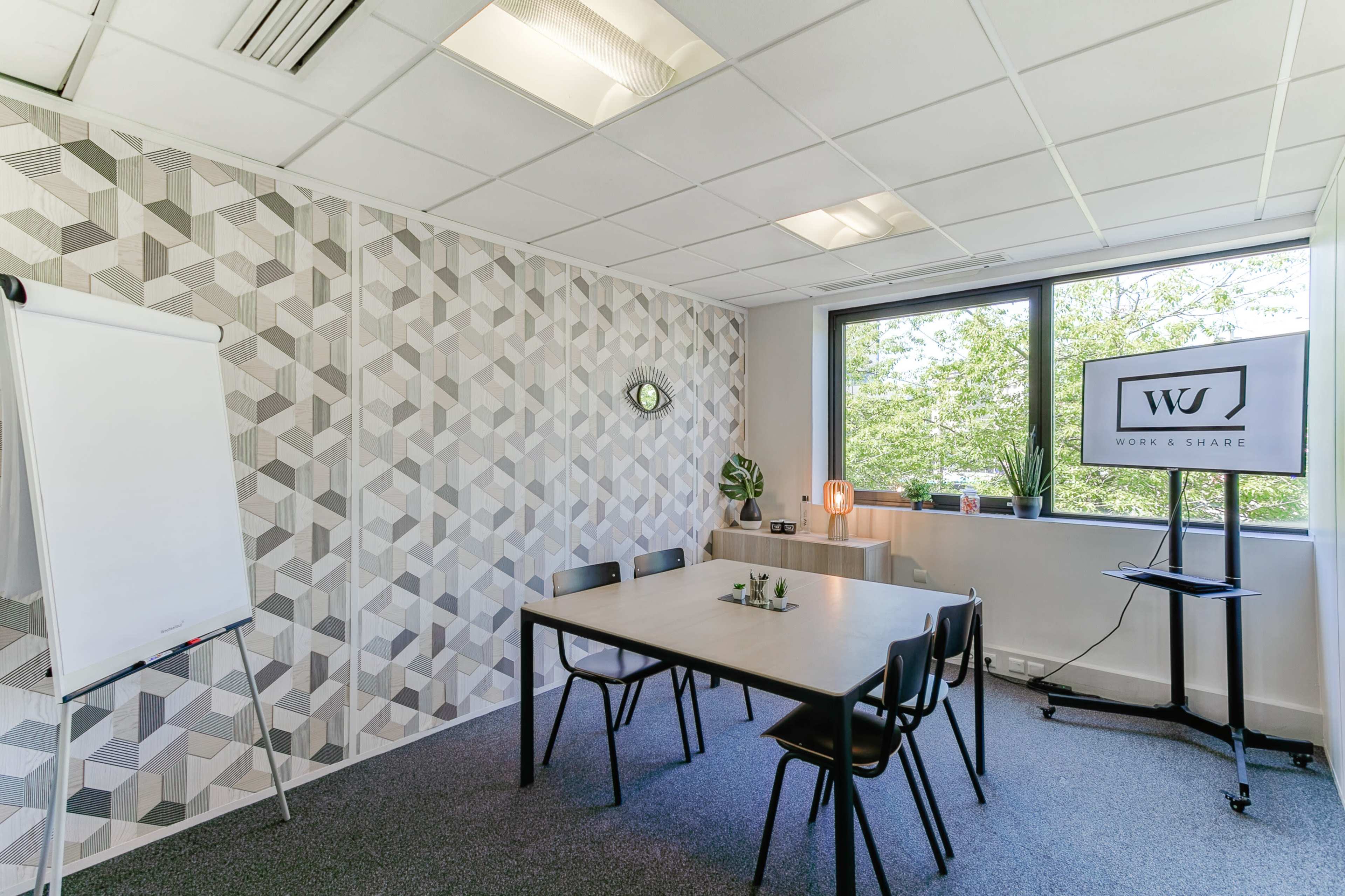 A modern meeting room with a geometric-patterned wall, a table with chairs, a whiteboard, and a screen displaying a logo.