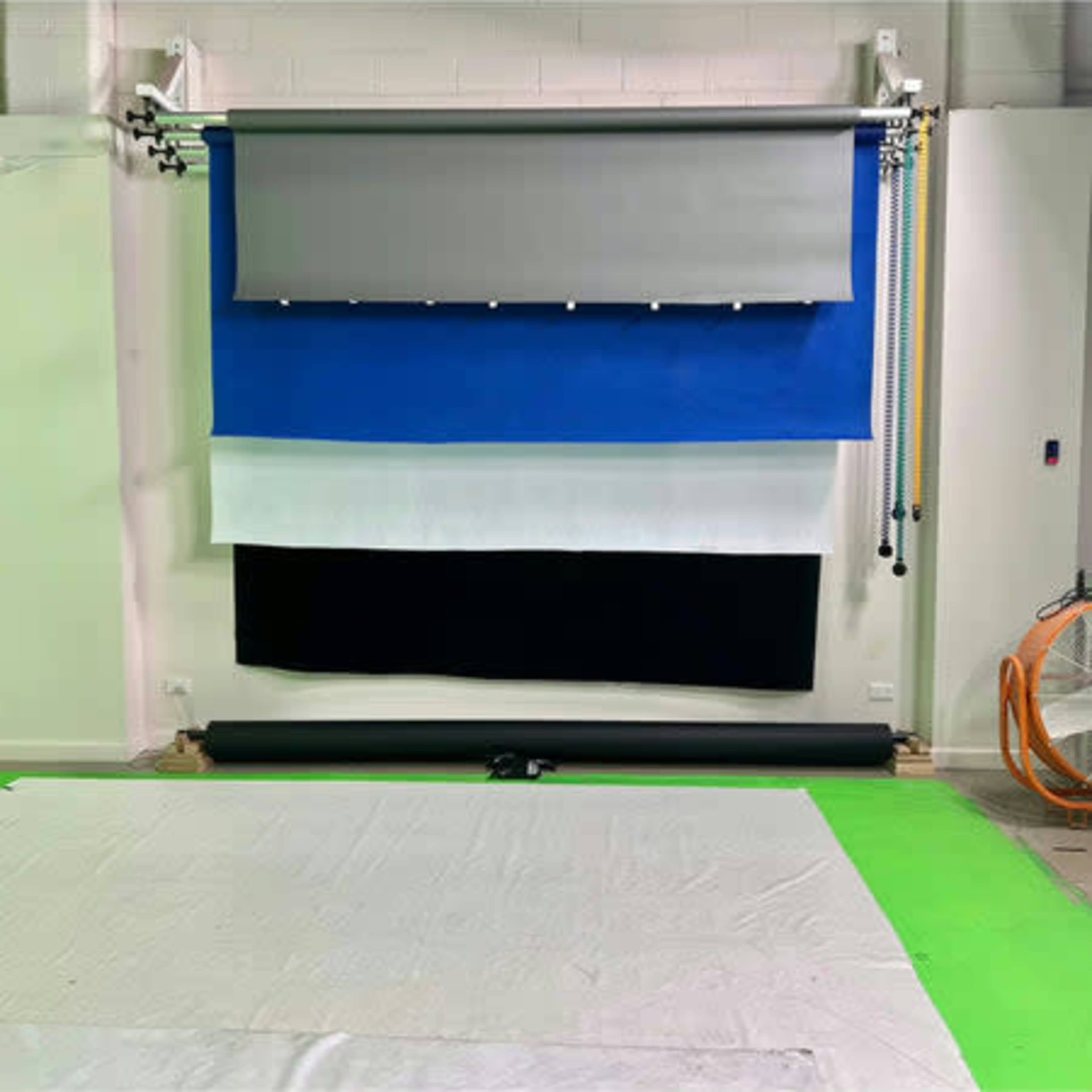 The image shows a backdrop setup in a studio with various colored cloths hanging vertically above a white and green floor covering.