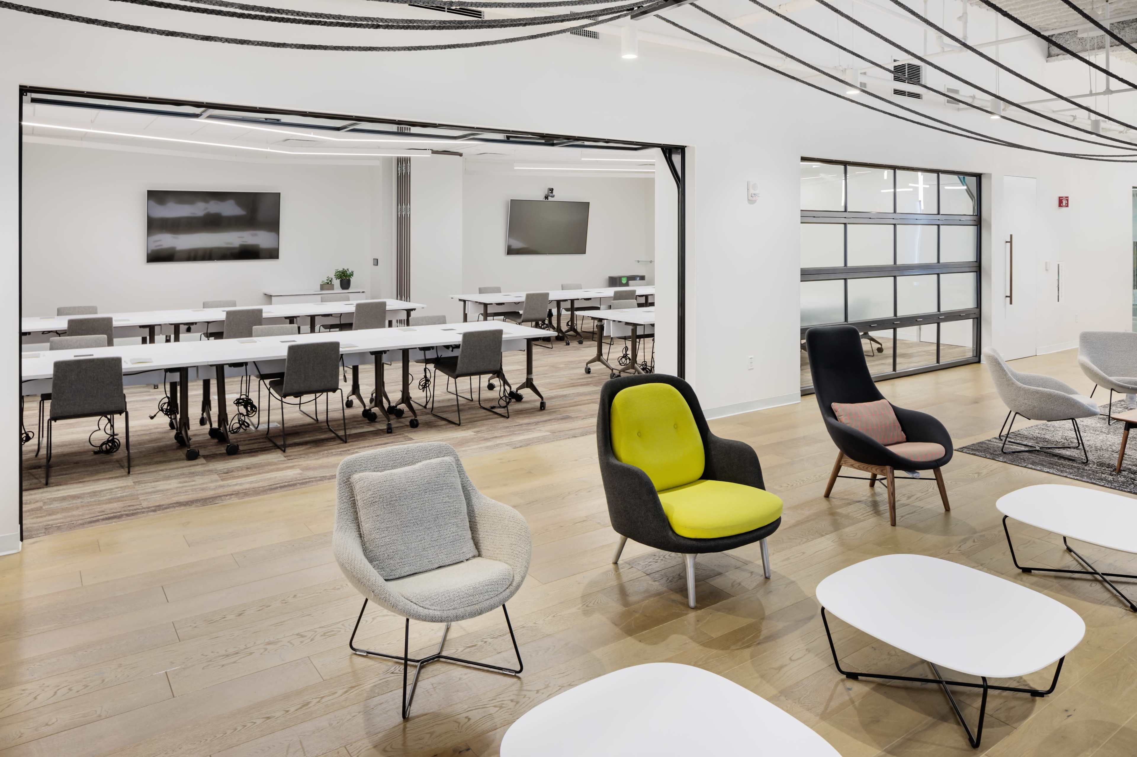 A modern office space with several tables and chairs set up for meetings, as well as a seating area featuring colorful lounge chairs.
